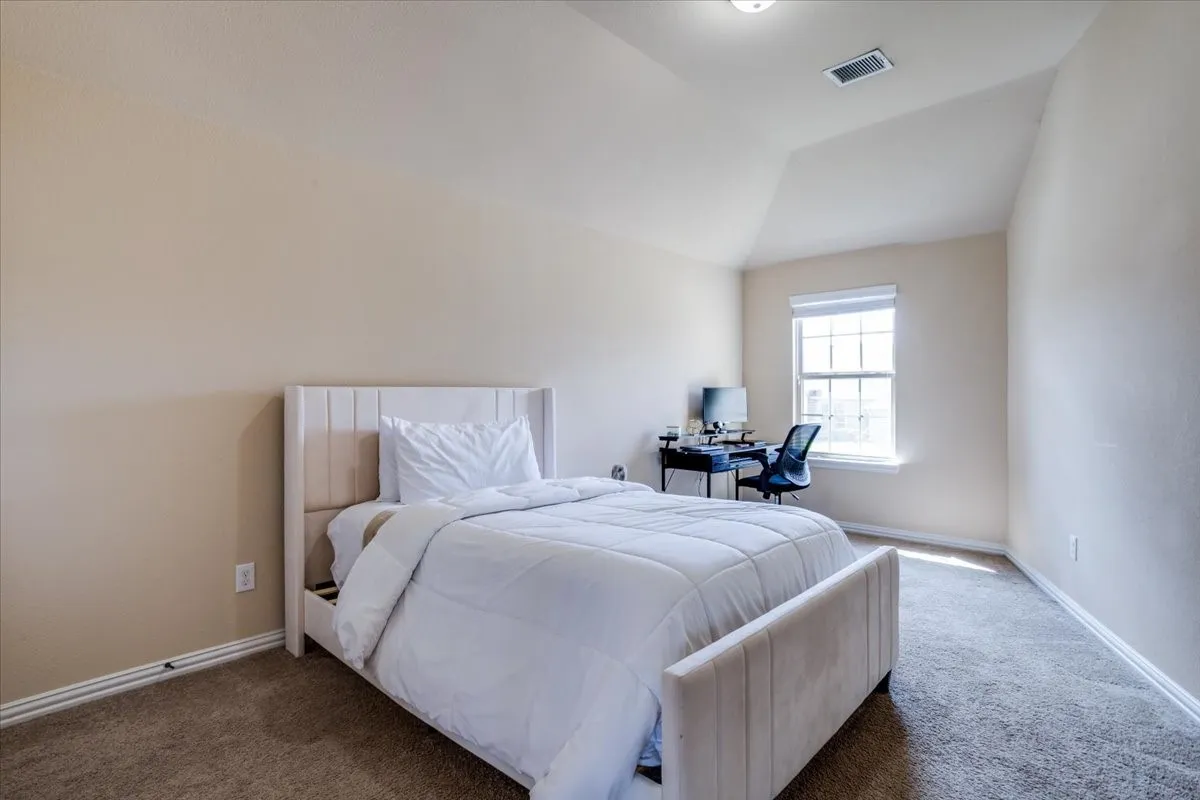 Carpeted bedroom featuring vaulted ceiling and an office area