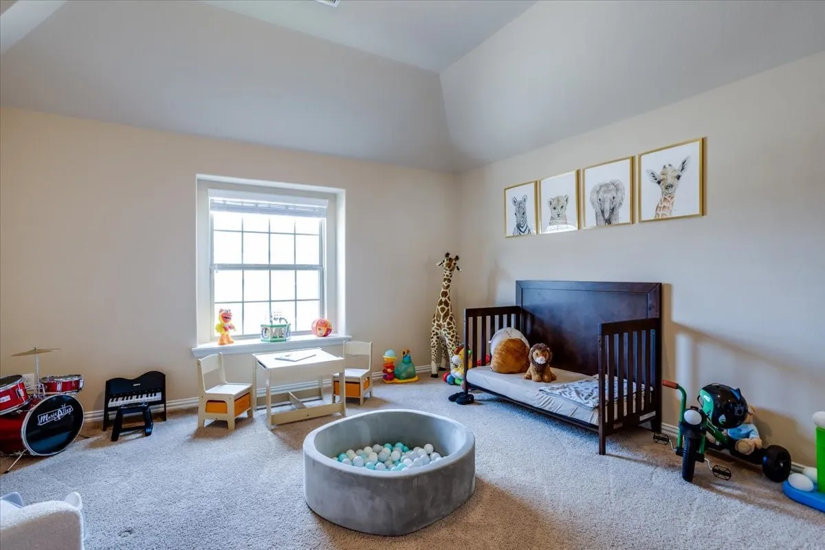 Bedroom with a crib, carpet flooring, and vaulted ceiling