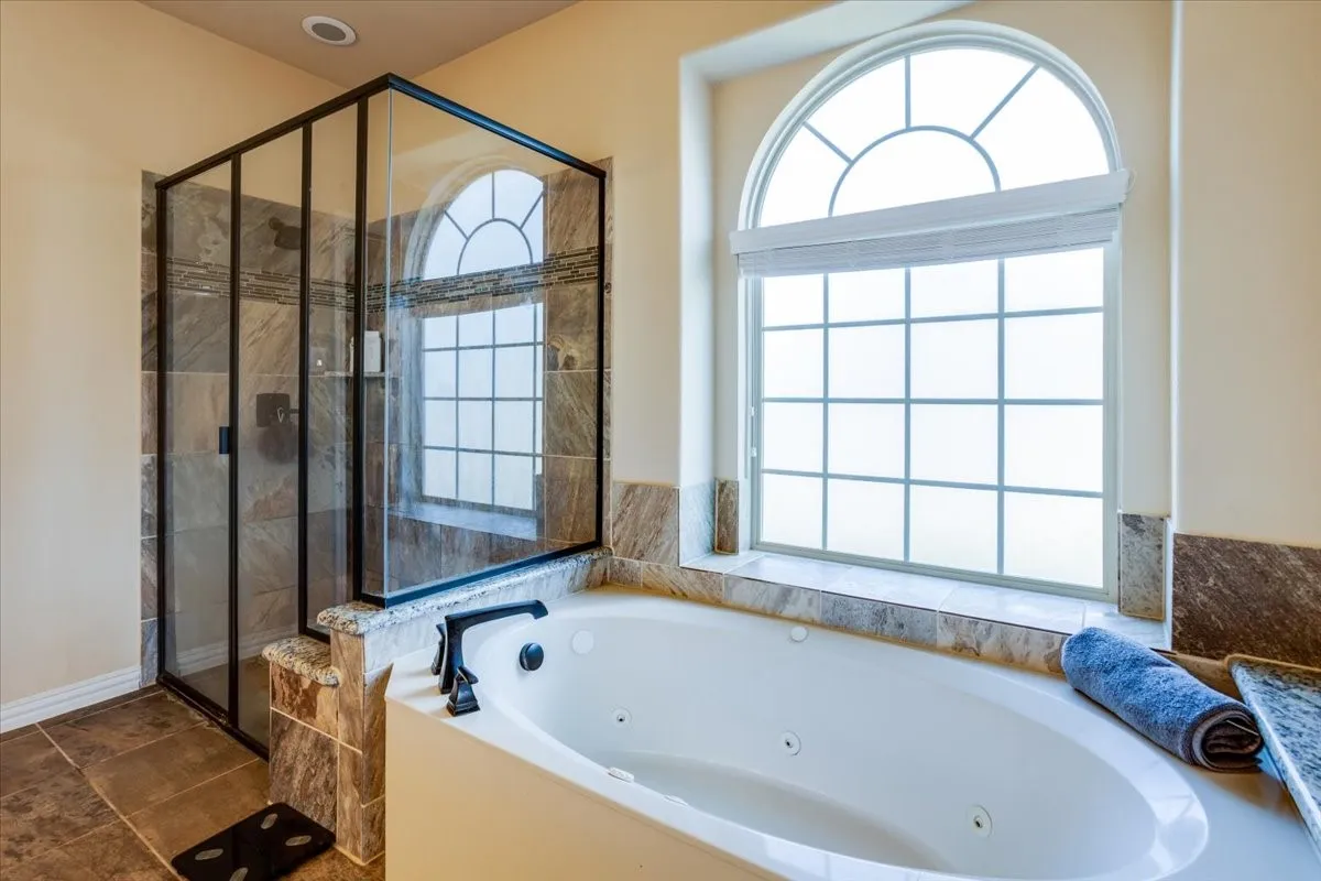 Bathroom with healthy amount of natural light, a stall shower, and a tub with jets
