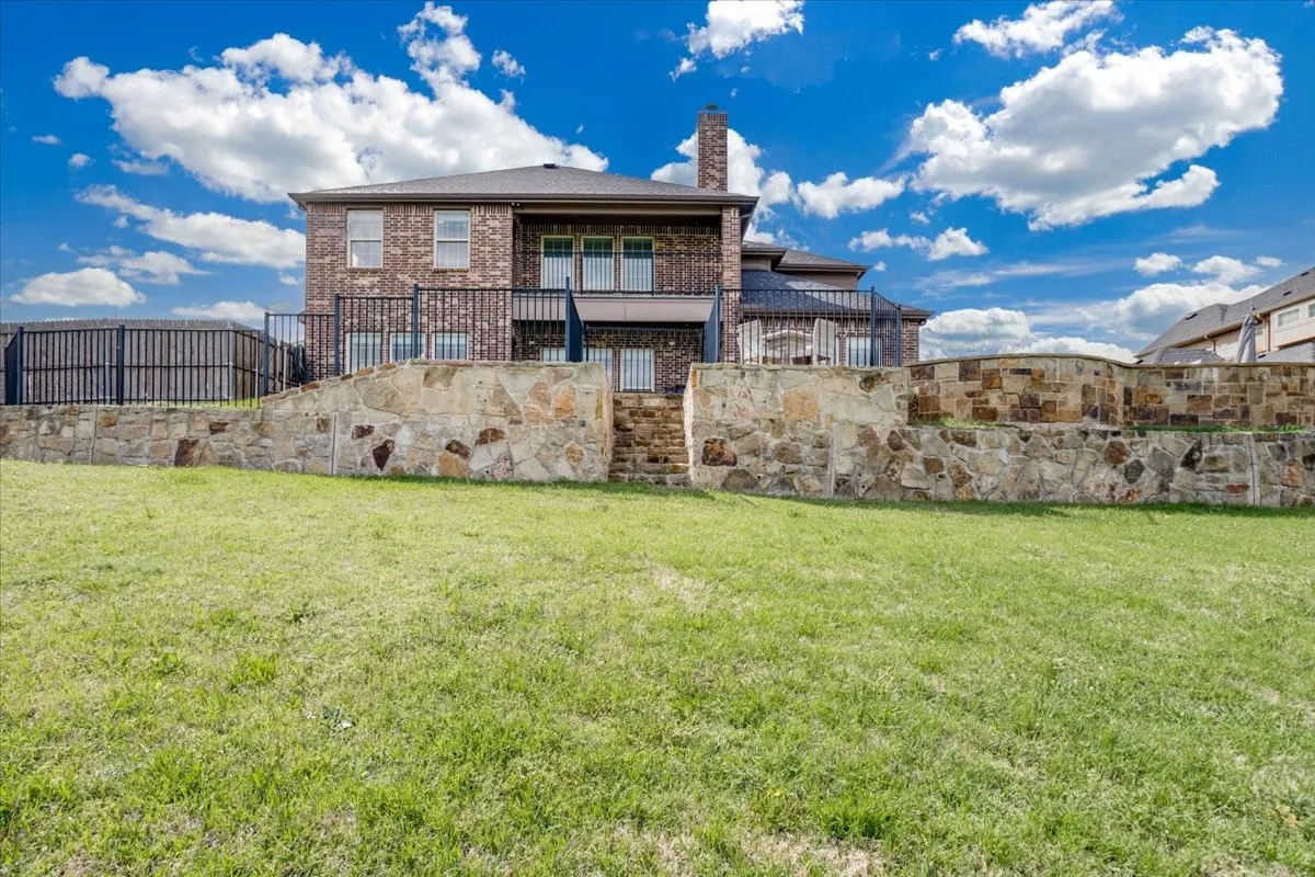 Back of property featuring a balcony, a yard, a chimney, and brick siding