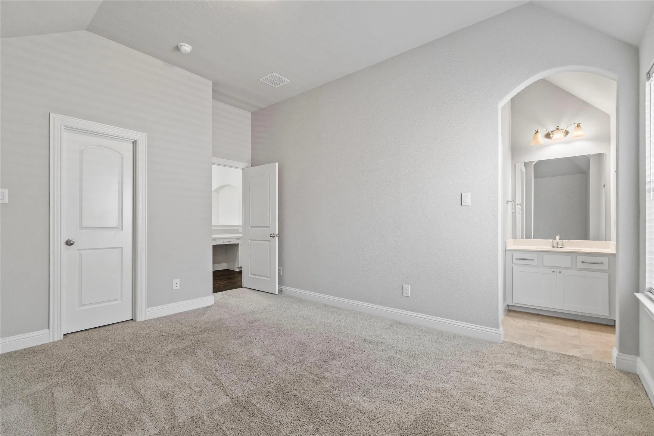 Unfurnished bedroom featuring vaulted ceiling, light colored carpet, and ensuite bathroom