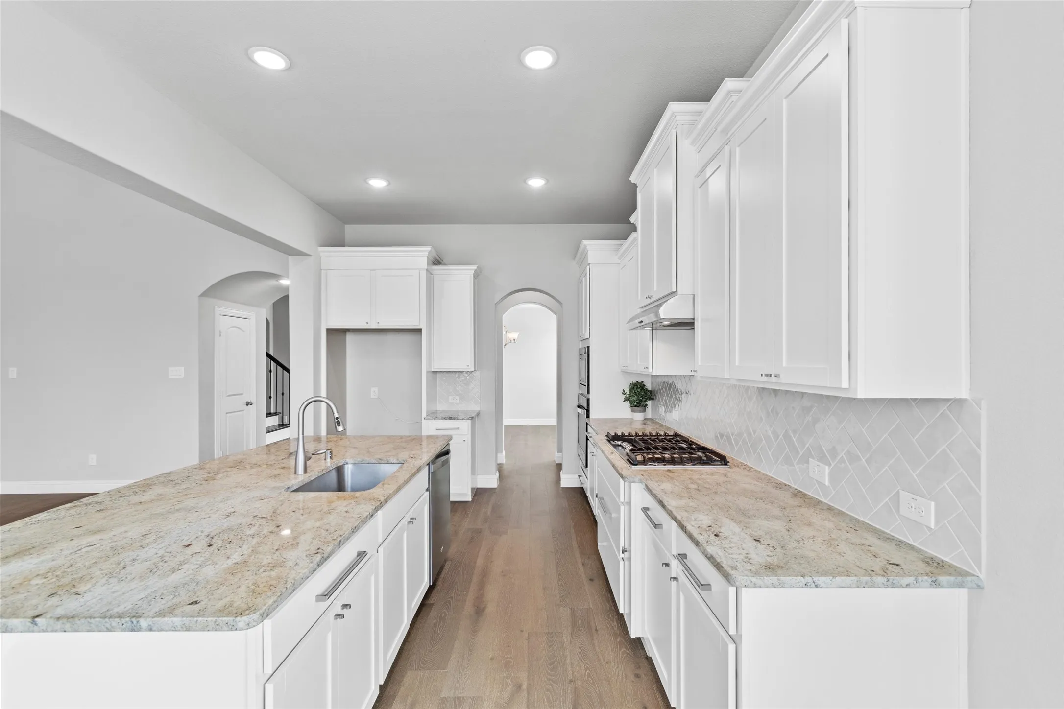 Kitchen with light wood-type flooring, white cabinets, backsplash, a kitchen island with sink, and sink