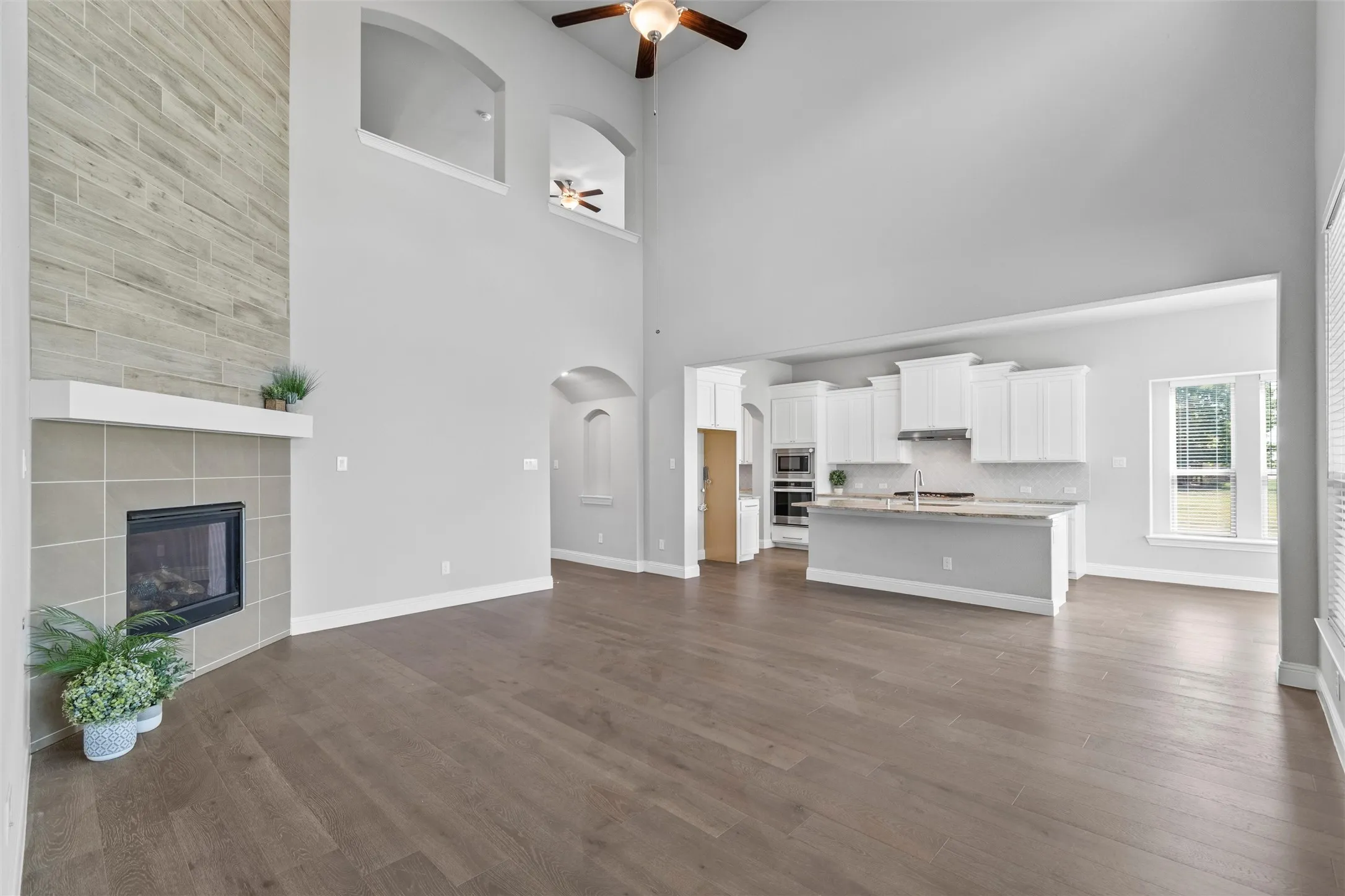 Unfurnished living room featuring a tile fireplace, a high ceiling, dark hardwood / wood-style floors, and ceiling fan