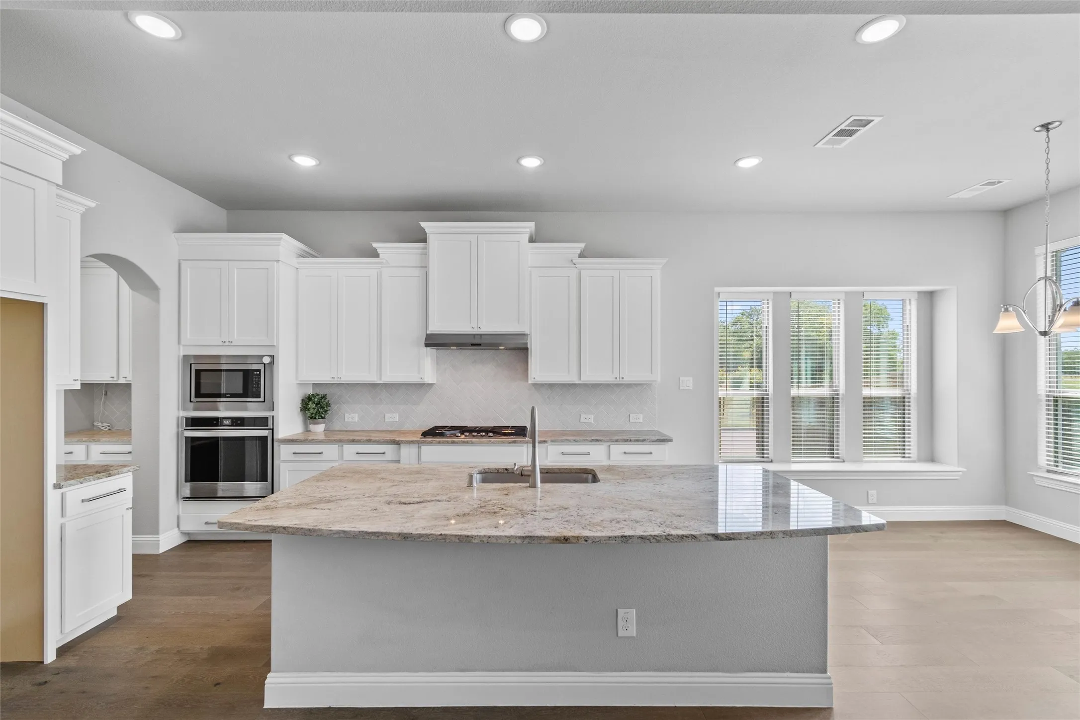 Kitchen with appliances with stainless steel finishes, light hardwood / wood-style flooring, sink, backsplash, and an island with sink