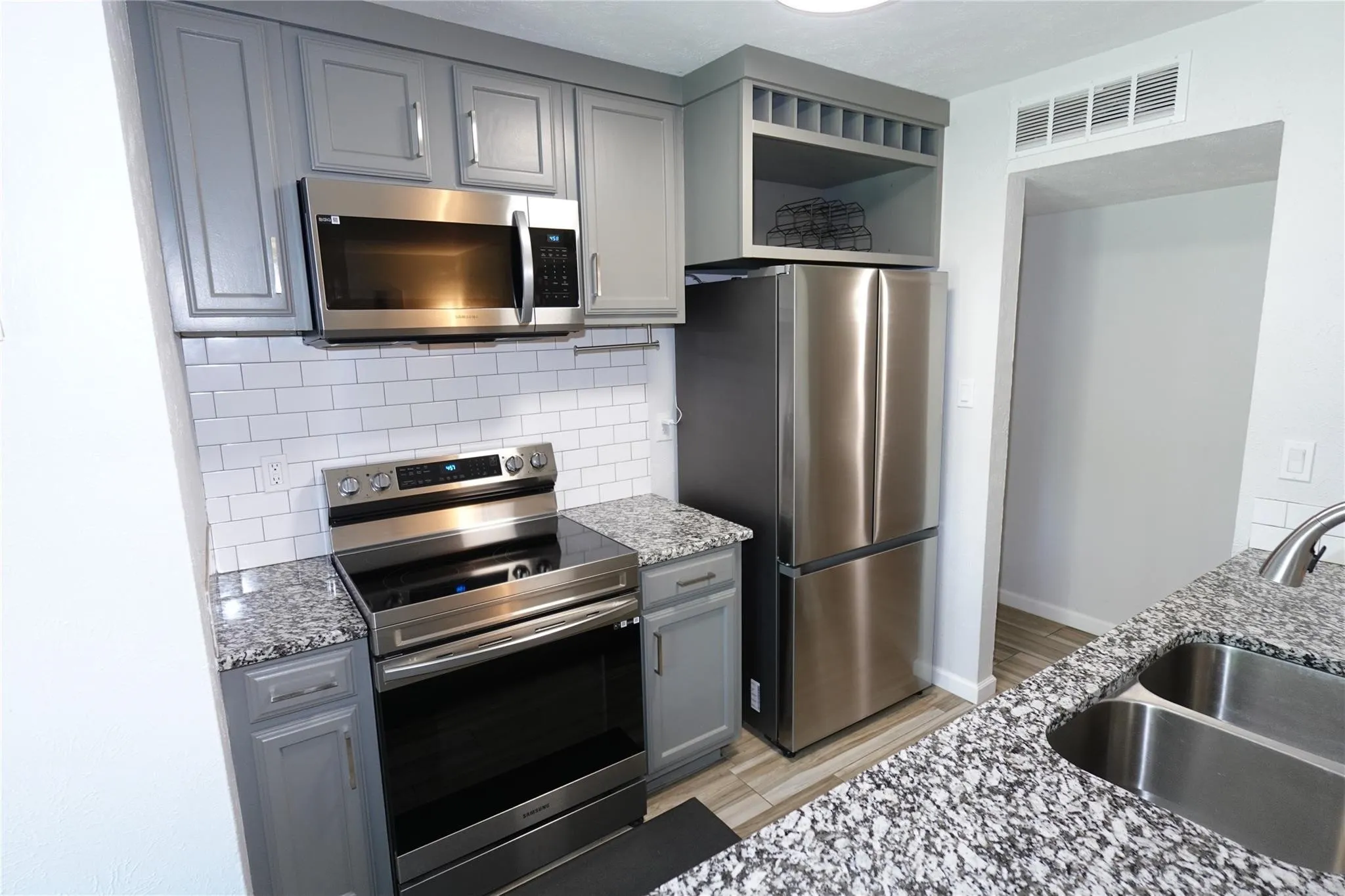 Kitchen featuring a double basin stainless steel sink, speckled countertops, stainless steel appliances including a microwave, oven, and refrigerator, gray cabinetry, and white subway tile backsplash