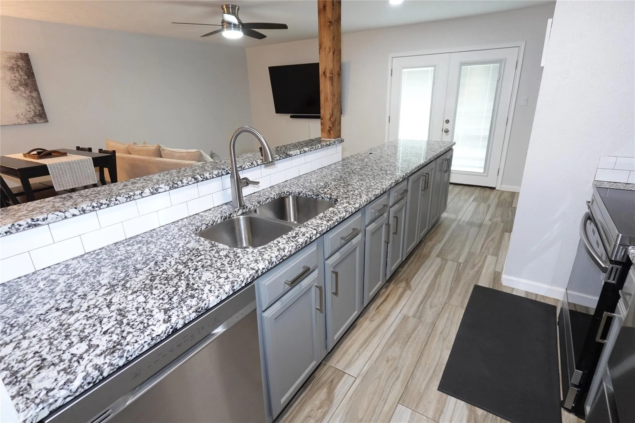 Kitchen featuring granite countertops, stainless steel double basin sink, stainless steel dishwasher, gray cabinetry, and wood-look flooring