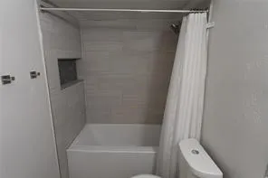 Bathtub and shower combination featuring light-toned tile surround and a recessed niche