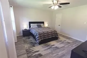 Spacious room featuring wood-finish flooring, a contemporary ceiling fan with integrated lighting, neutral wall tones, and a white interior door