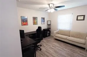 Spacious room featuring wood-finish flooring, a ceiling fan with integrated lighting, and a window with horizontal blinds