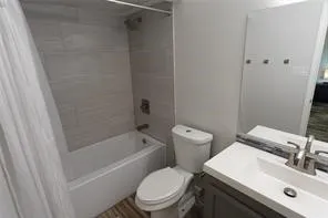 Bathroom featuring a white porcelain tub, light-toned horizontal tile surround, a single toilet, and a vanity with an integrated sink and brushed nickel faucet