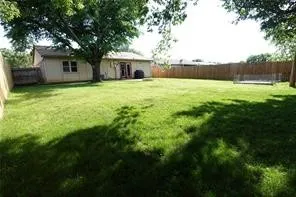 Expansive backyard featuring a manicured lawn, established mature trees, a full wood privacy fence, and a neutral-toned exterior with double patio doors