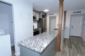 Kitchen featuring a granite countertop island, stainless steel appliances, and wood-finish flooring
