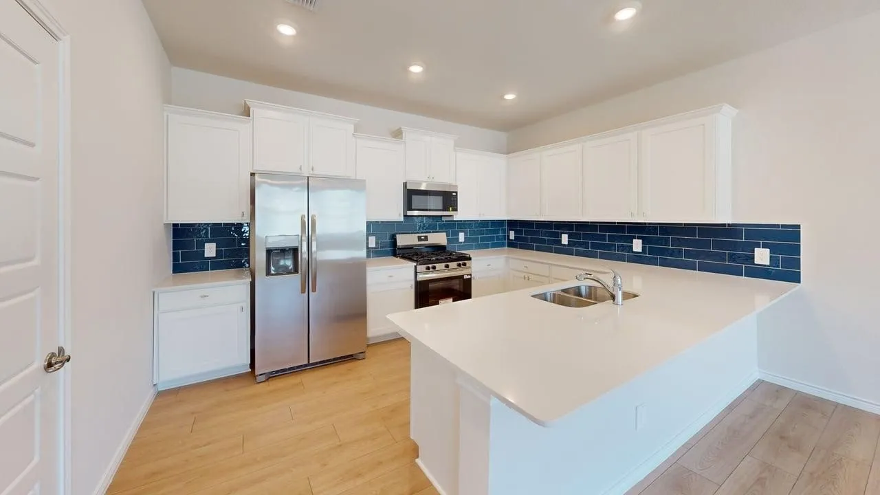 Contemporary kitchen featuring white cabinetry, a large kitchen island with an undermount double-basin sink, stainless steel appliances, and a bold blue subway tile backsplash