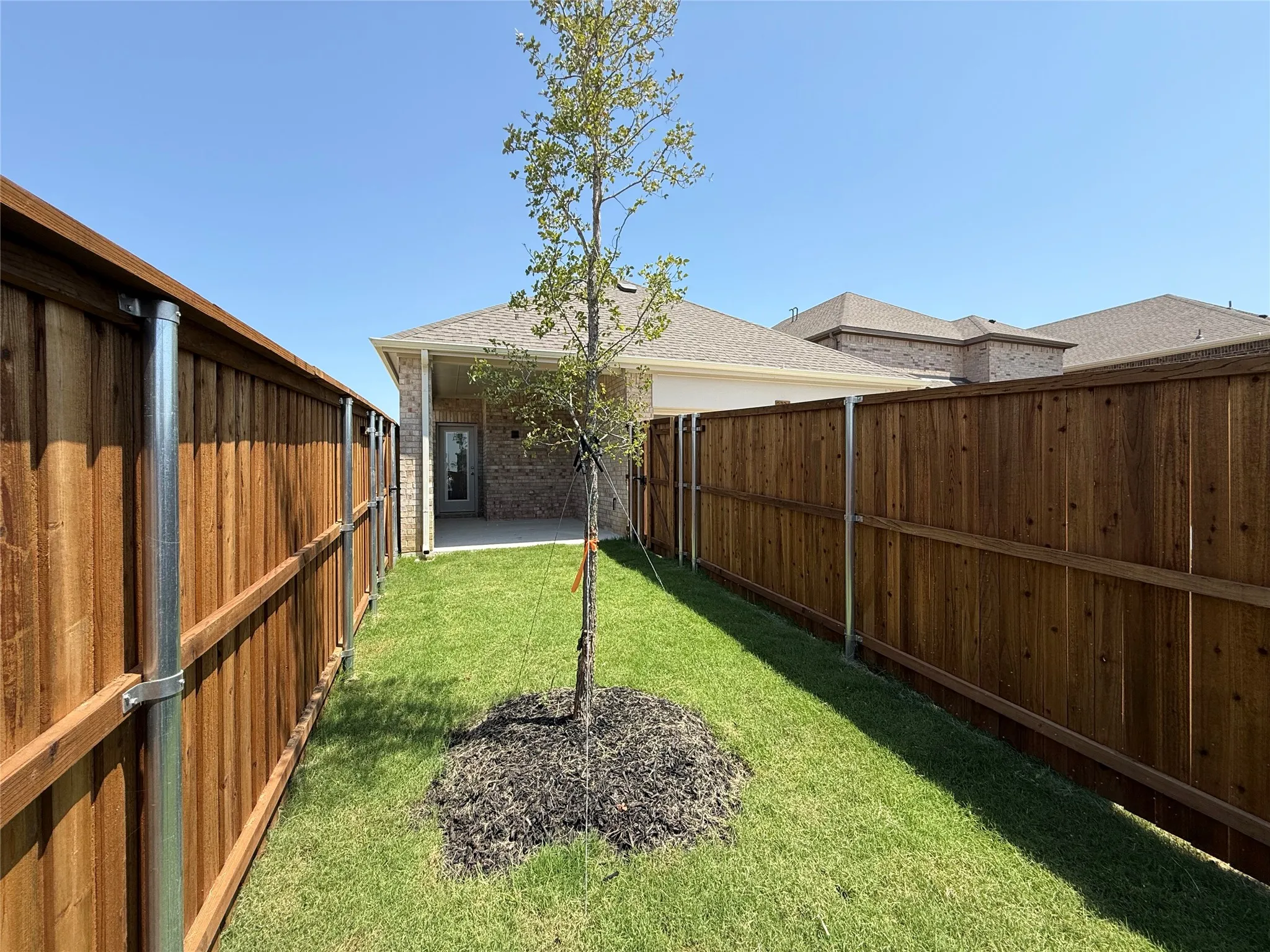 Private backyard featuring a manicured lawn, established tree, and wood privacy fencing with metal posts
