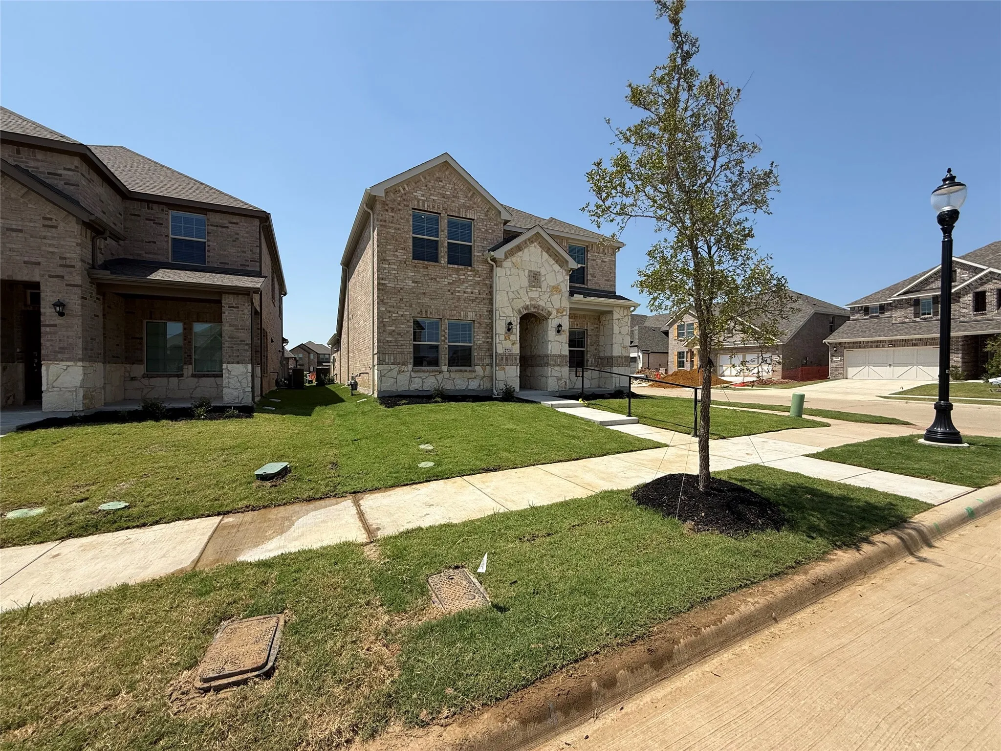 Two-story residence featuring a brick and stone facade, covered entry, and a newly installed lawn