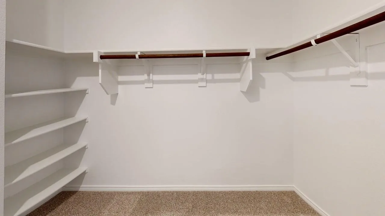 Walk-in closet featuring built-in shelving, dual hanging rods, and neutral-toned carpeting