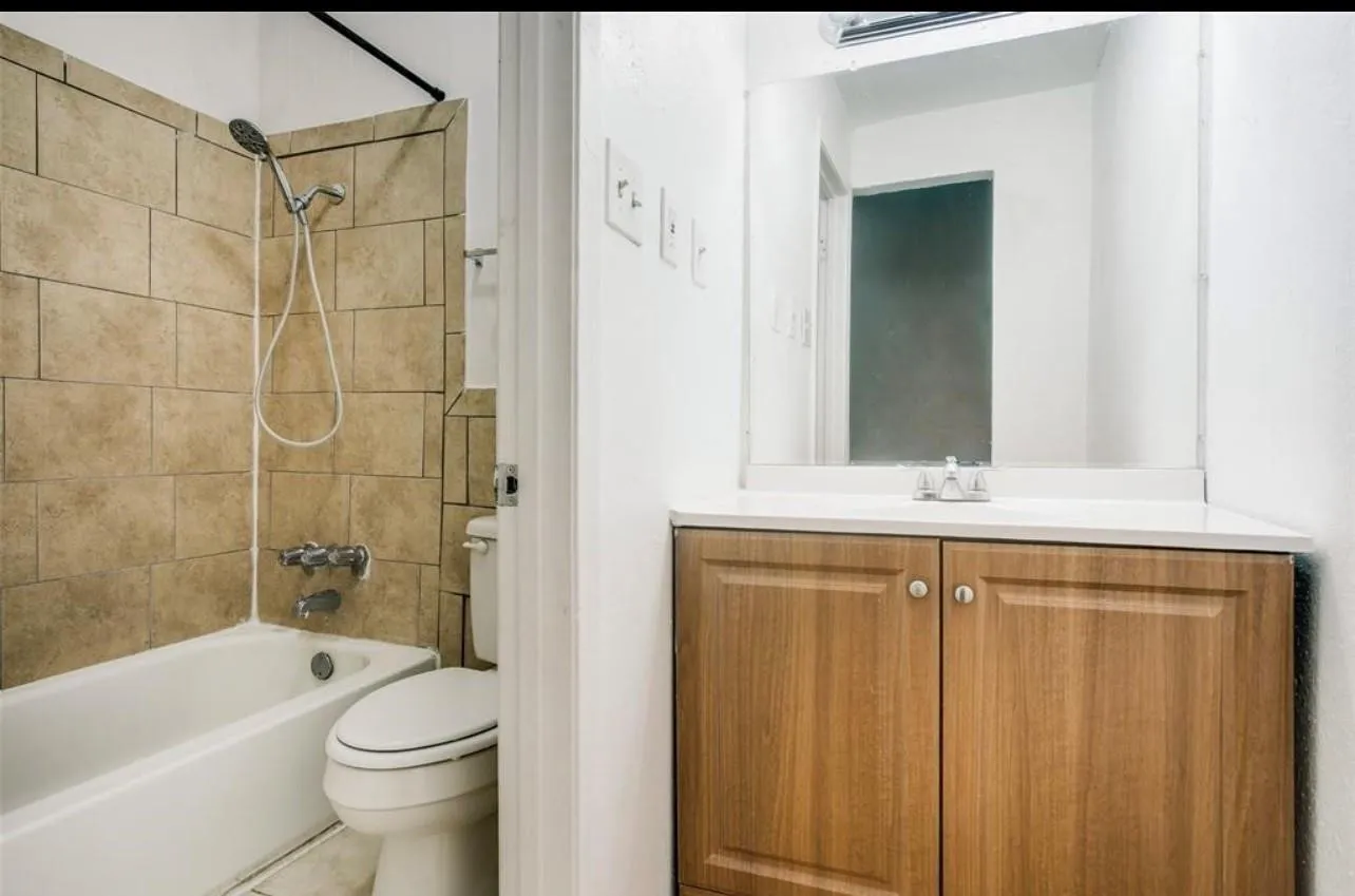 Bathroom featuring a ceramic tile bath surround, white bathtub, wall-mounted mirror, and a wood-finish vanity with a light-colored countertop