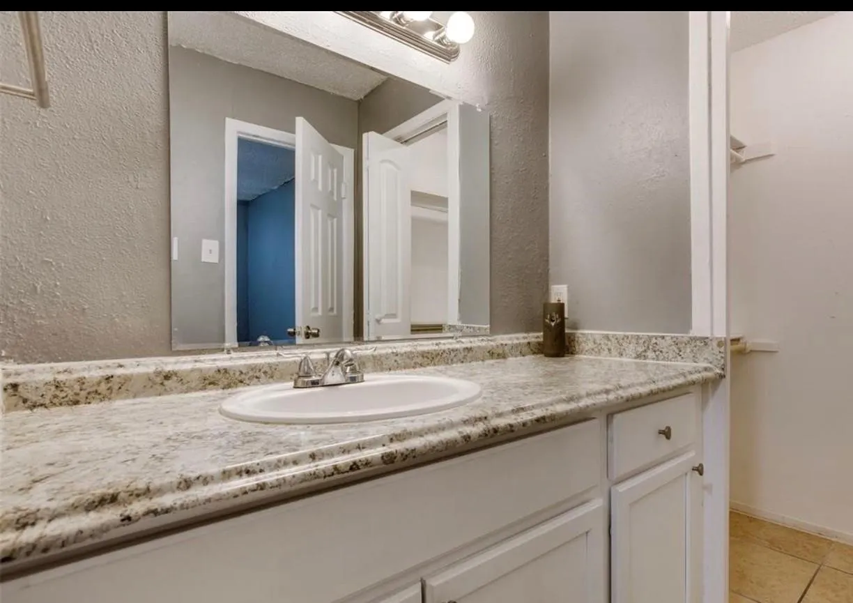 Bathroom vanity featuring a speckled countertop, white cabinetry, undermount sink, and chrome faucet