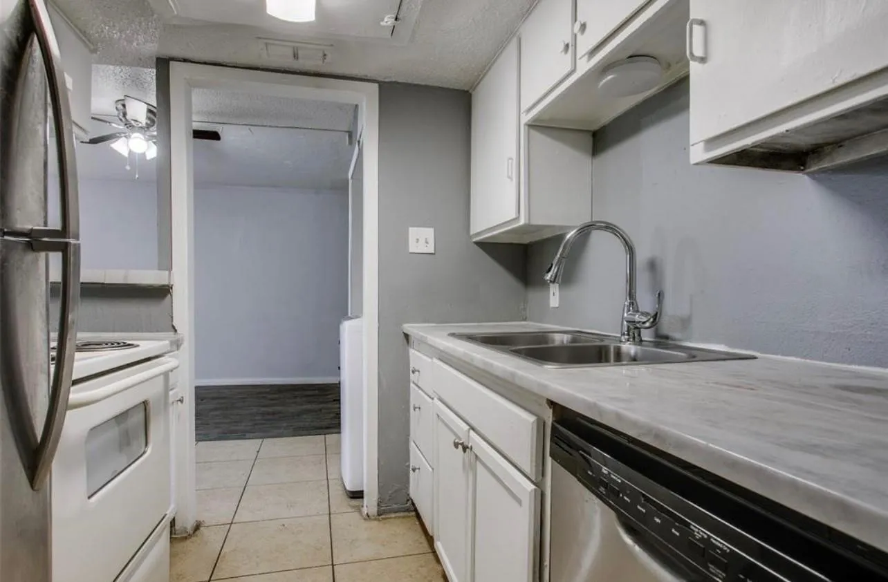 Kitchen featuring stone-finish countertops, stainless steel dual-basin sink with gooseneck faucet, white cabinetry, and tile flooring