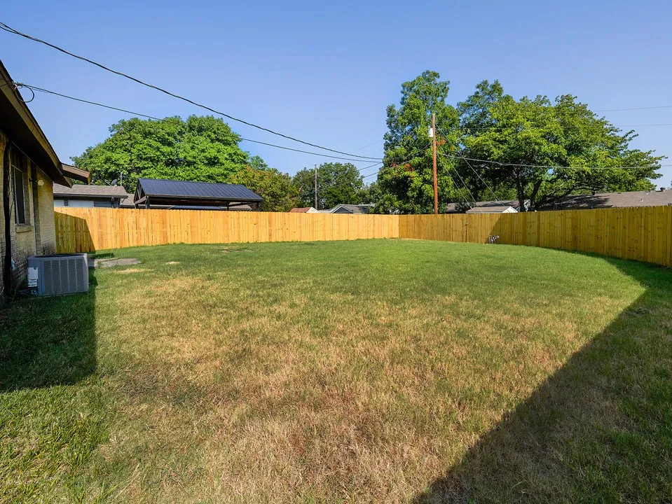 Expansive backyard featuring a level lawn bordered by wood privacy fencing, mature shade trees, and clear sightlines across the grounds