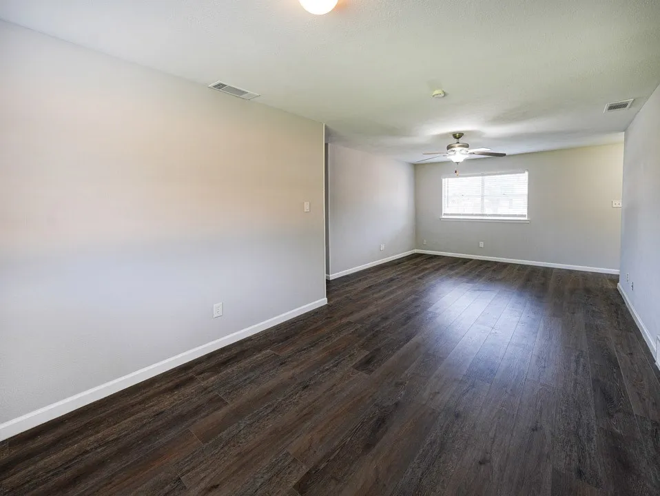 Wood-finish flooring, neutral wall tones, ceiling fan with integrated lighting, and multiple windows