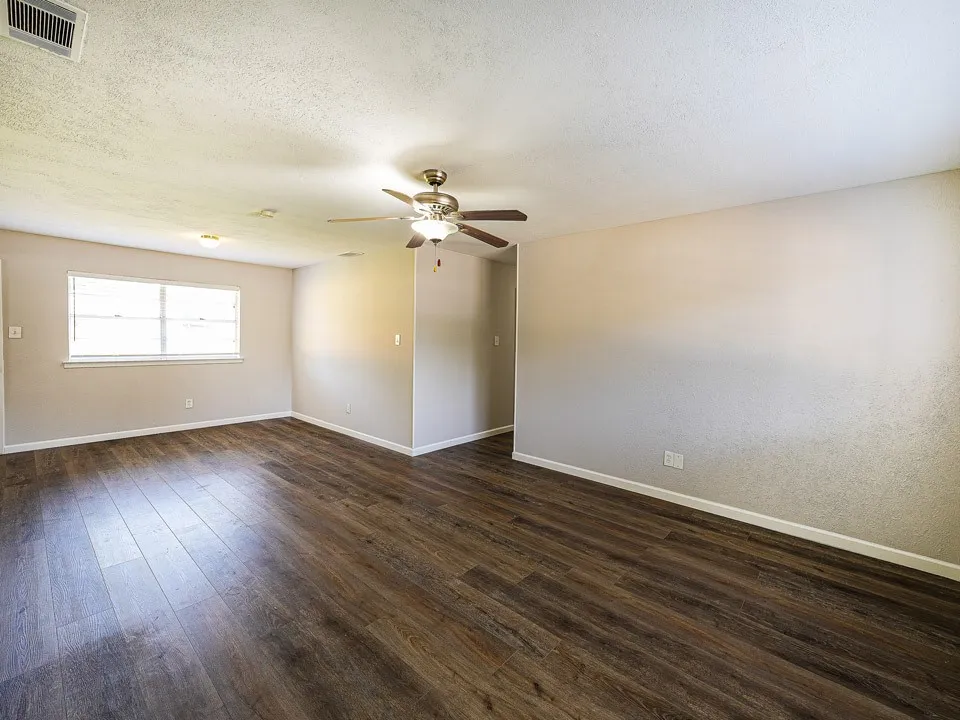 Spacious room featuring wood-finish flooring, neutral-toned walls, a ceiling fan with integrated lighting, and a multi-pane window