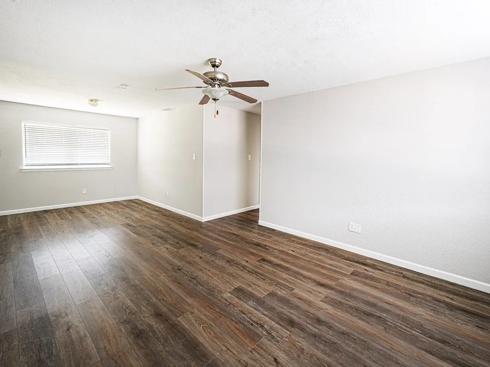 Spacious living area showcasing wood-finish flooring throughout, neutral wall finishes, and abundant natural light from a large window