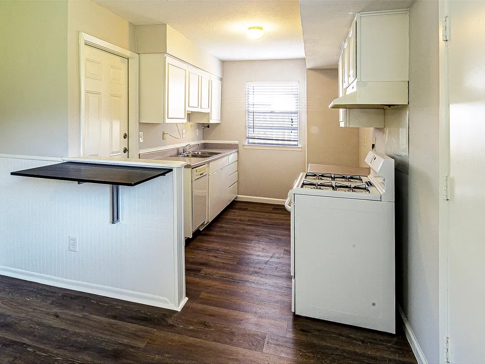 Kitchen featuring wood-finish flooring, white cabinetry, a built-in breakfast bar, a gas range, and a window for natural light