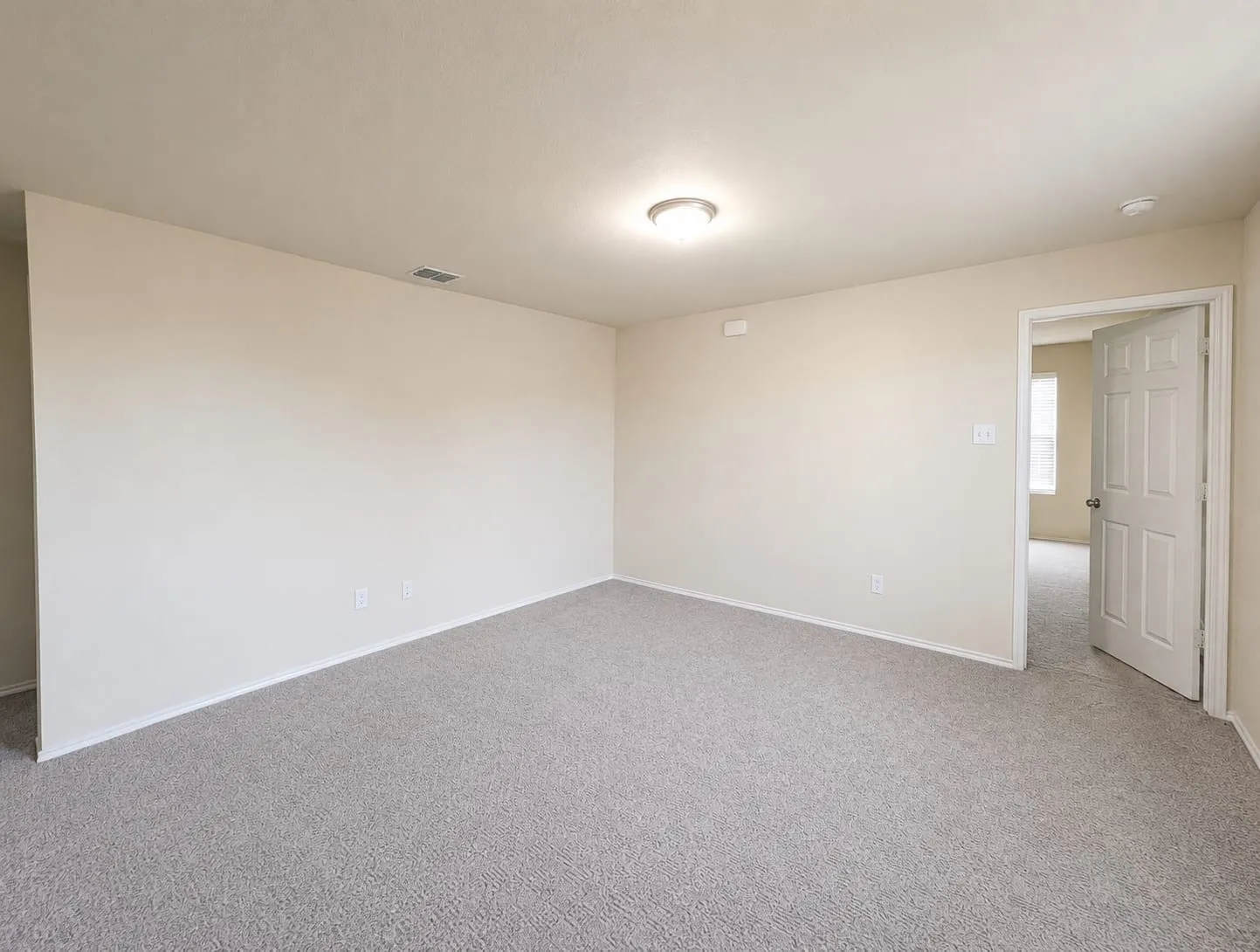 Spacious interior room with light beige walls and new grey carpeting