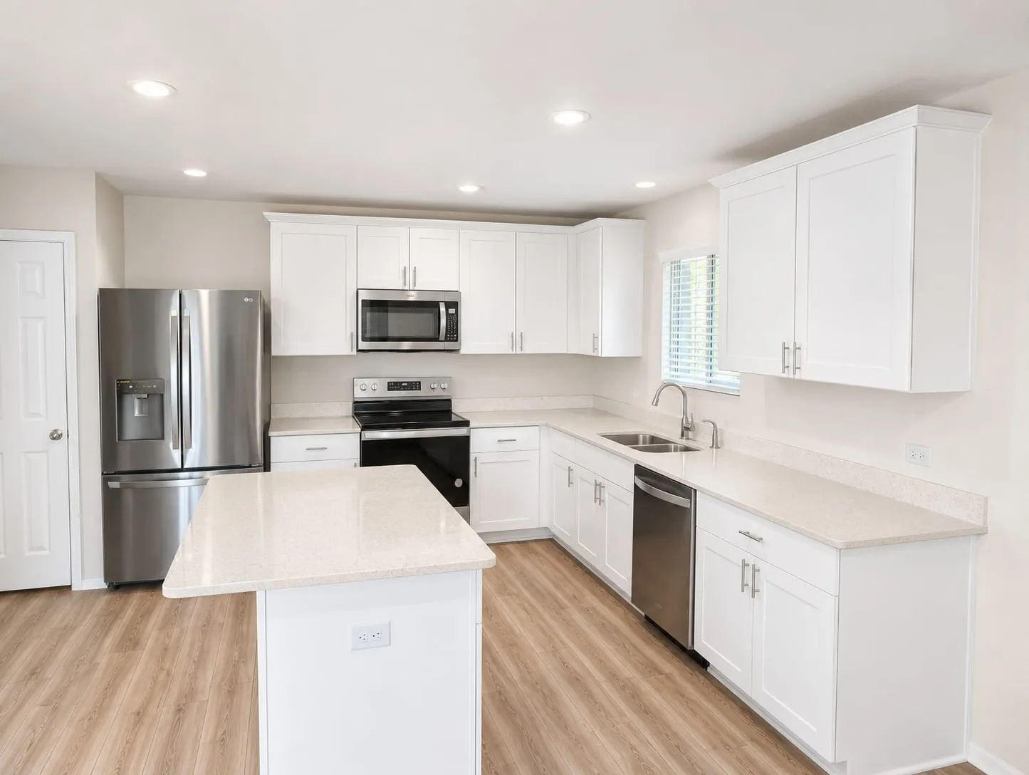 Modern kitchen featuring white shaker cabinetry, stainless steel appliances, light-toned countertops, a central island, and wood-finish flooring