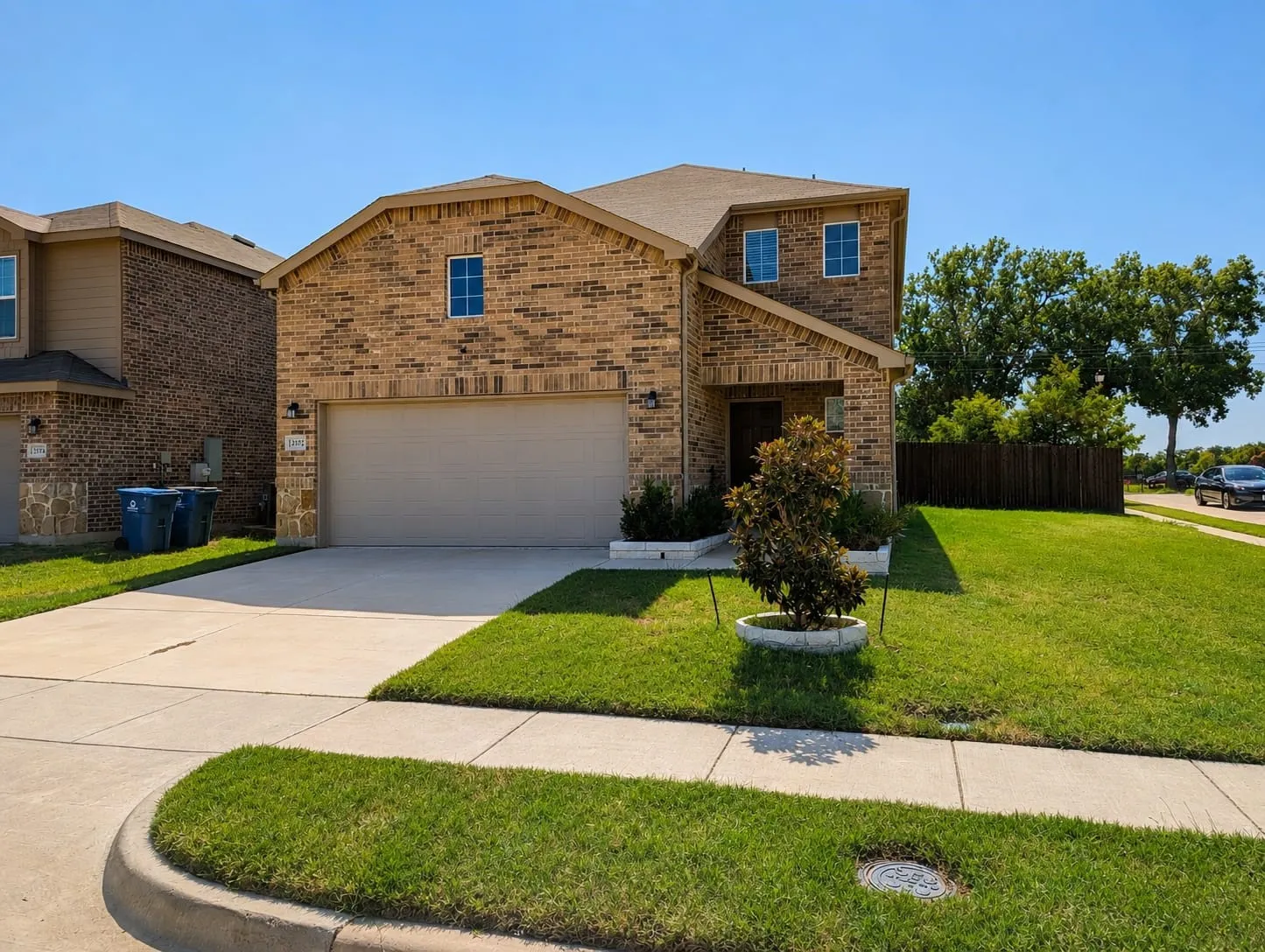 Two-story brick exterior with an attached garage, concrete driveway, and established front lawn