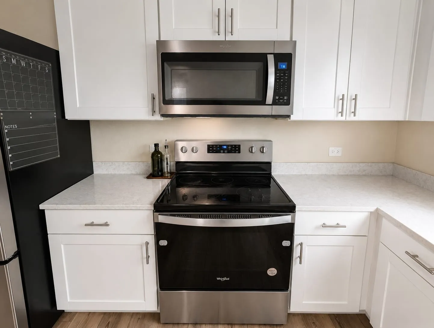 Modern kitchen featuring white shaker cabinetry, light-toned countertops, and stainless steel appliances including a range and microwave