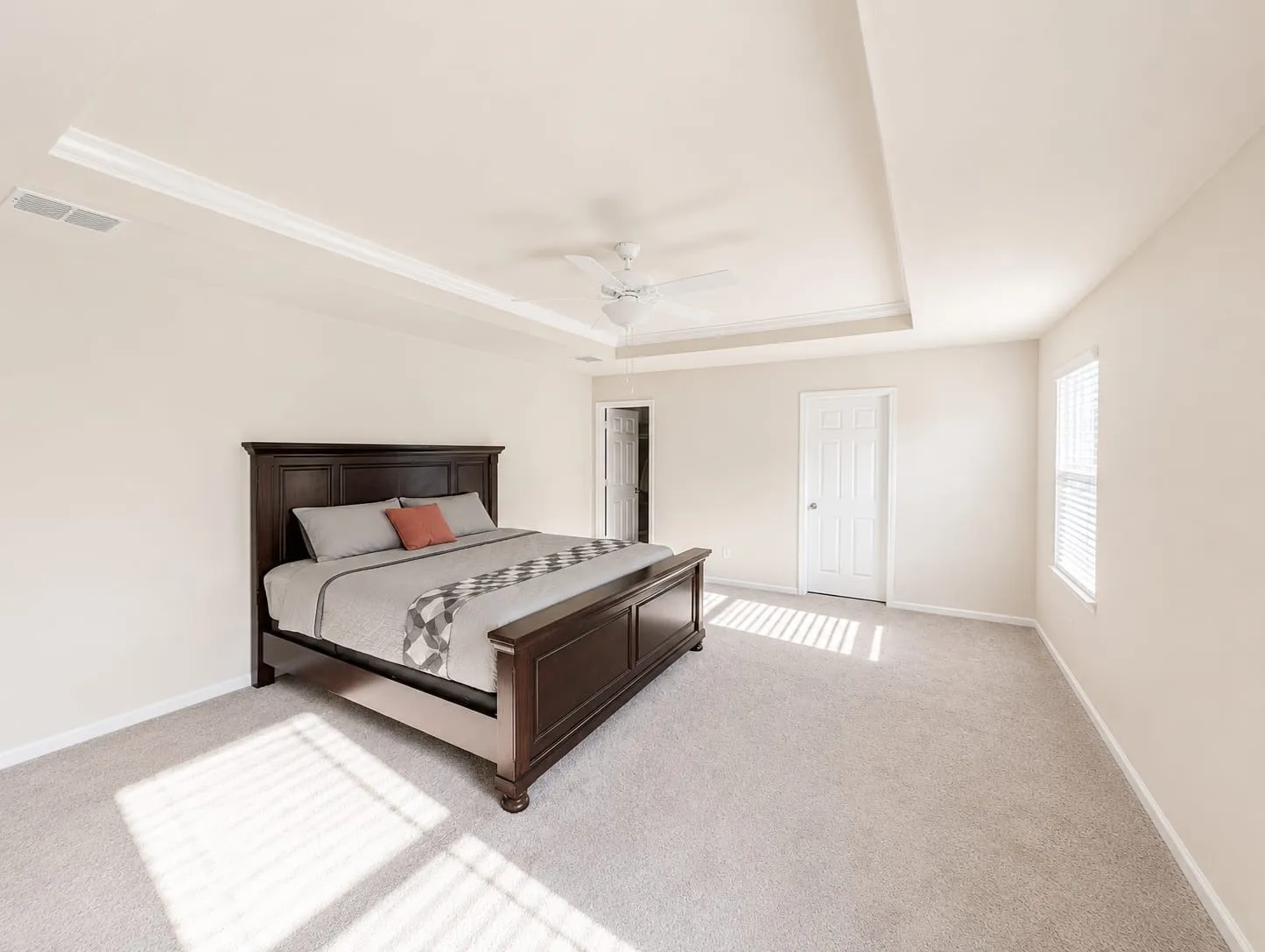 Spacious room featuring neutral carpeting, a tray ceiling with crown molding, and a ceiling fan