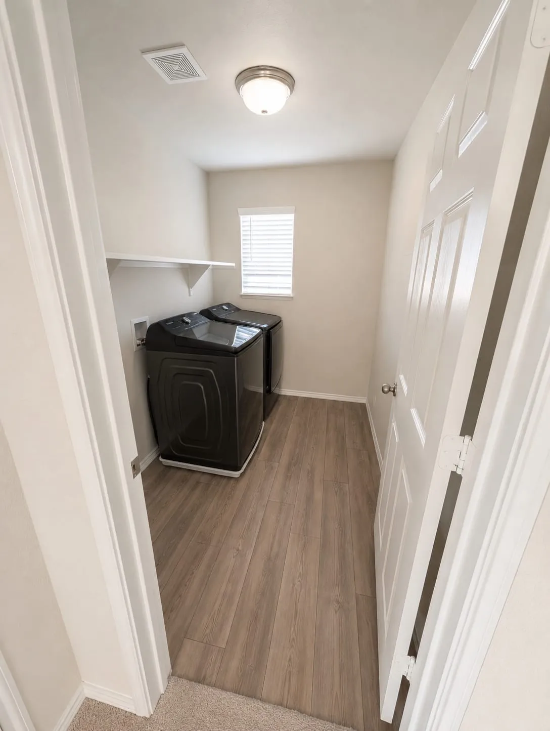Dedicated laundry room featuring wood-finish flooring, a white shelving unit, and a window with horizontal blinds