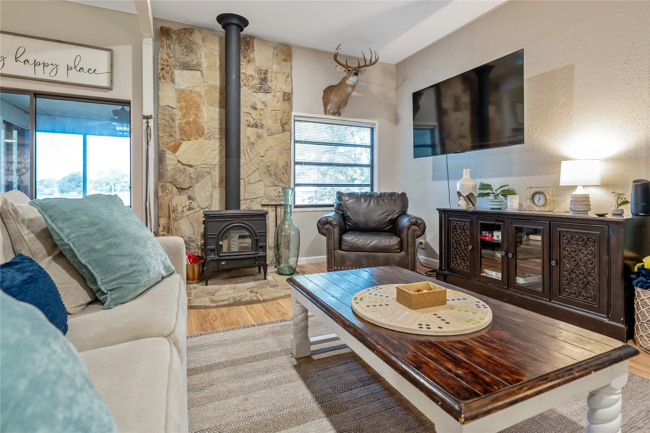 Living area featuring a stone accent wall with a black wood-burning stove and chimney pipe, wood-finish flooring, and a large sliding glass door