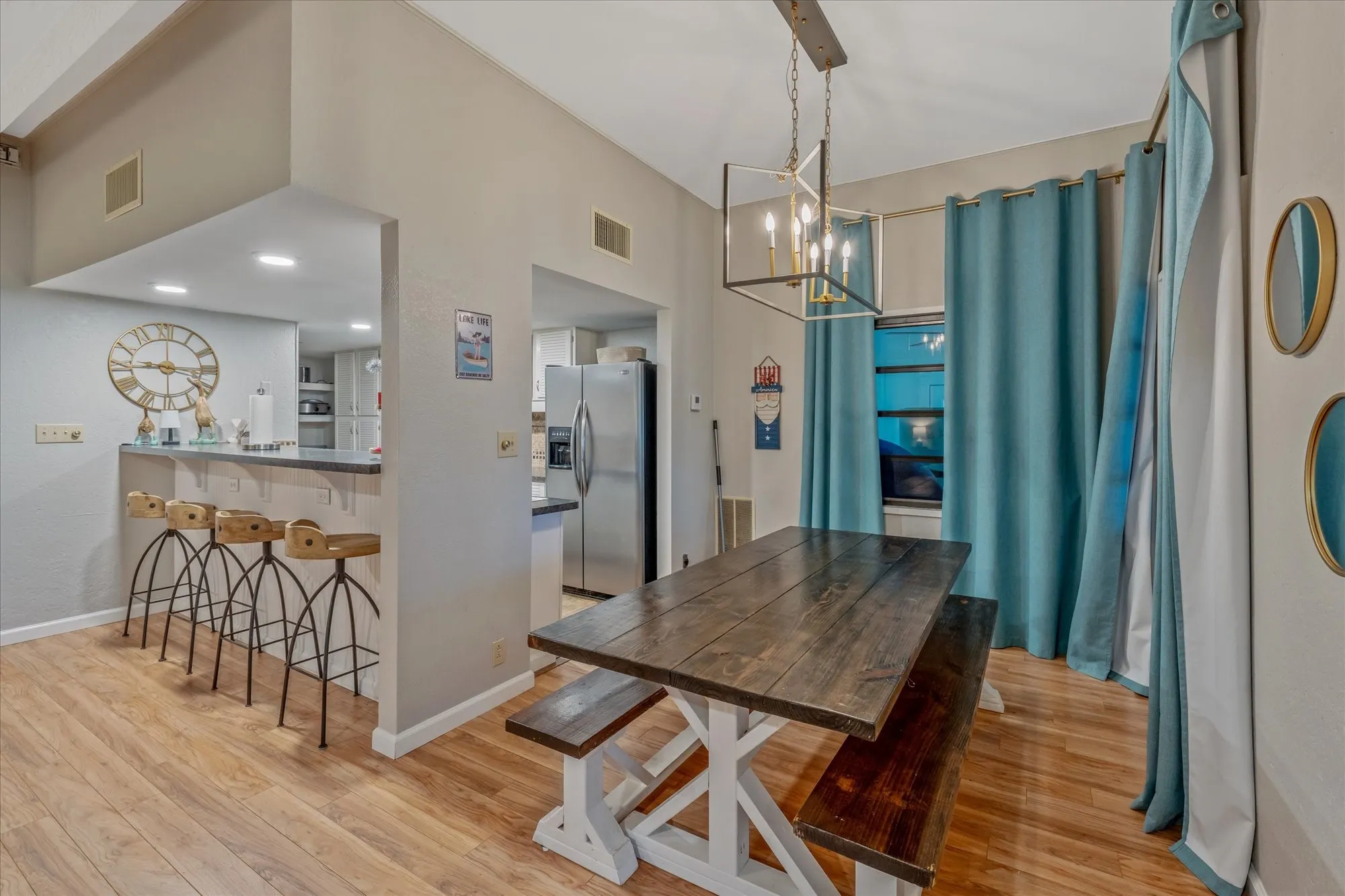 Dining area featuring wood-finish flooring, a contemporary chandelier, a pass-through bar with seating, and window treatments