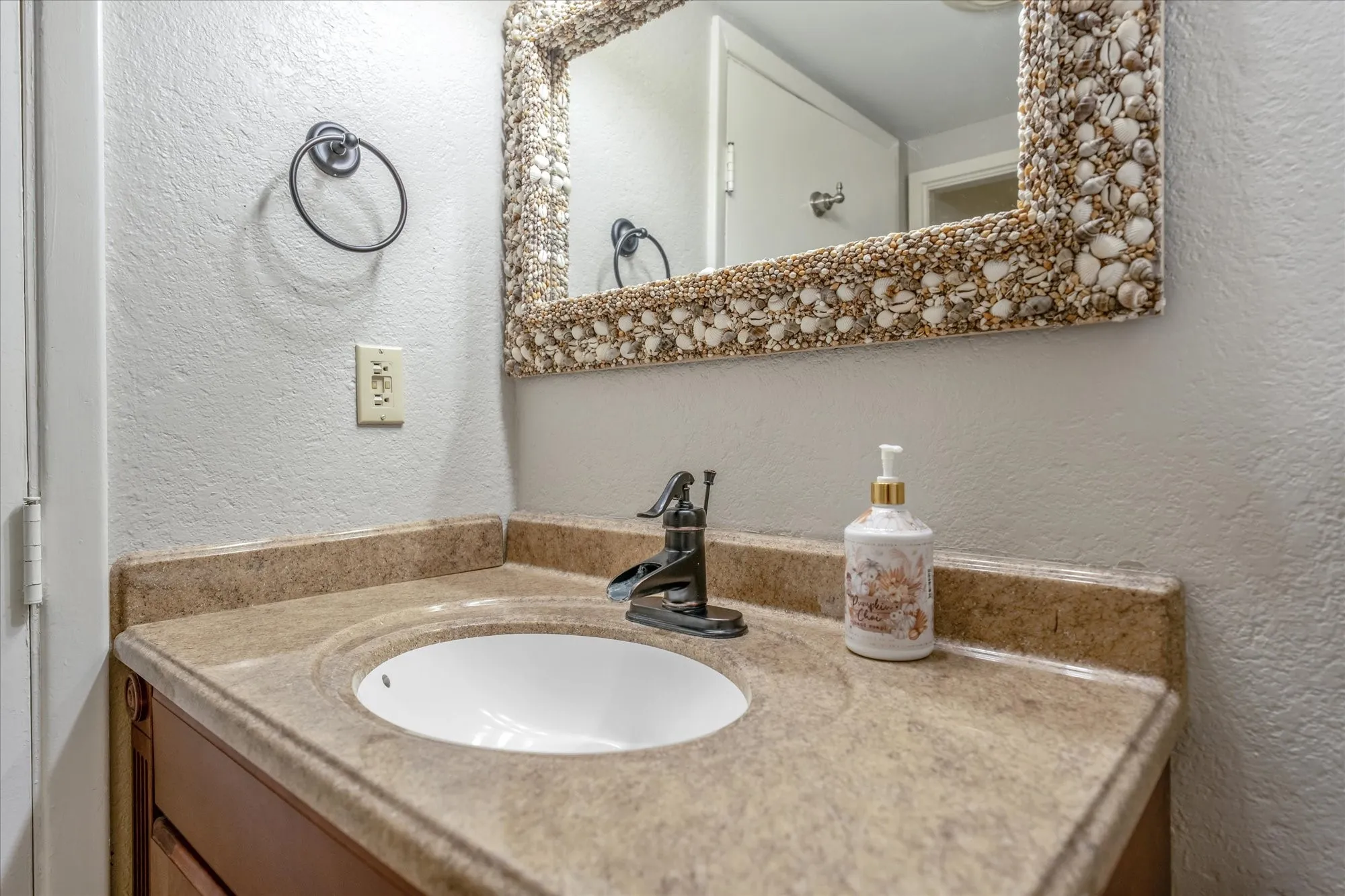 Bathroom vanity featuring a shell-adorned mirror, integrated sink, and bronze-finish faucet