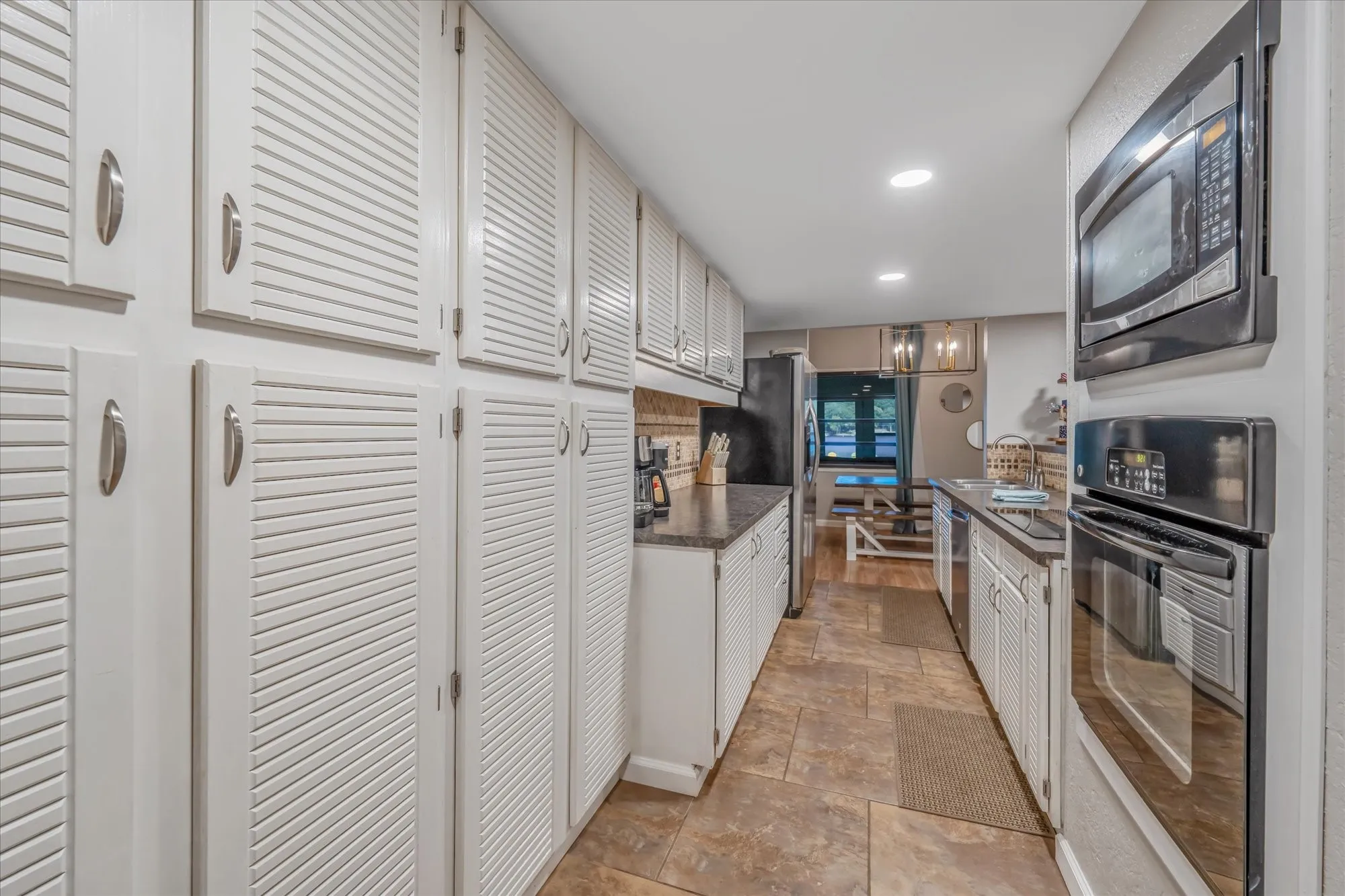 Galley kitchen featuring extensive white louvered cabinetry, stone-finish countertops, and matching tile flooring