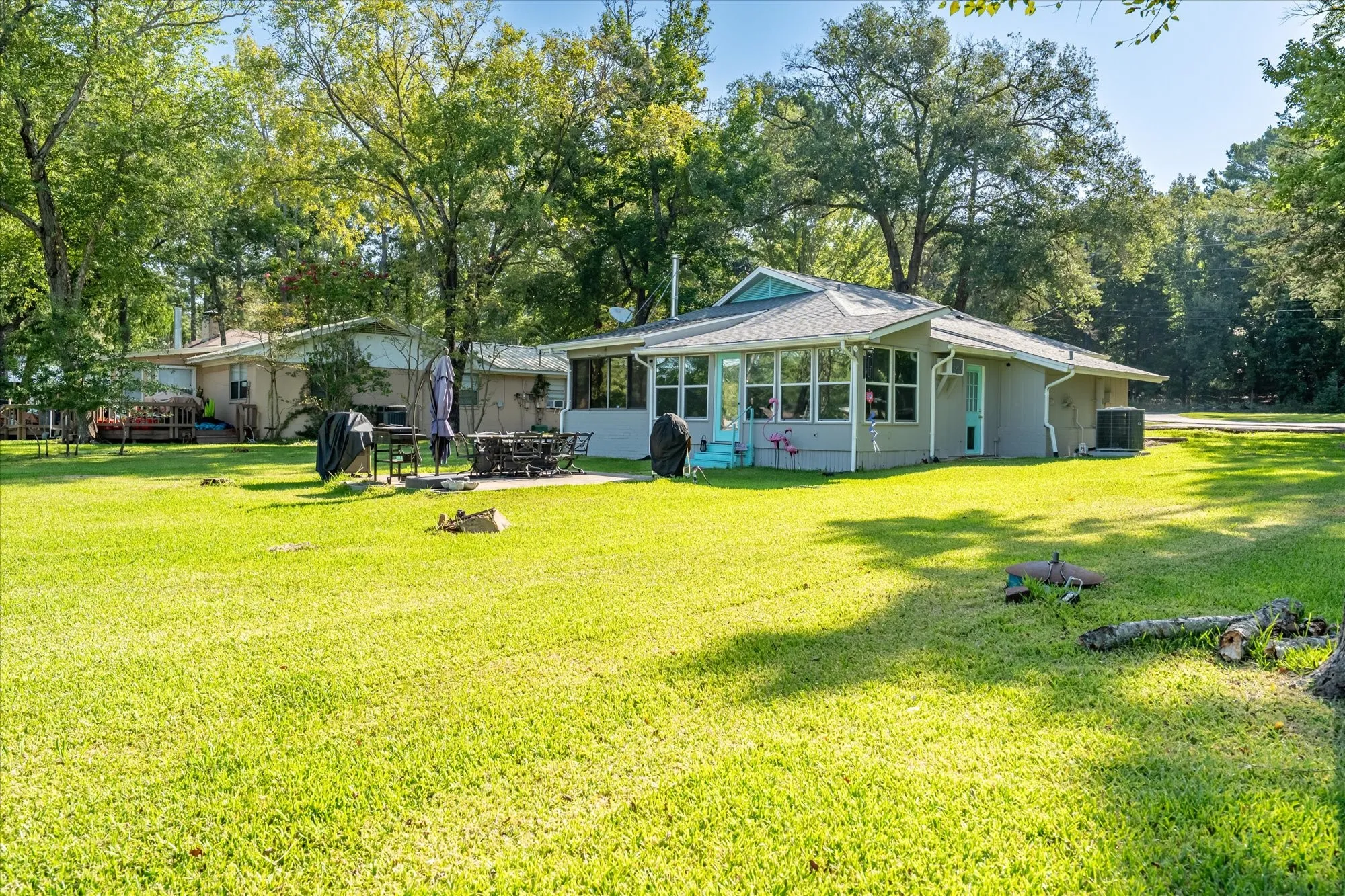 Spacious lawn surrounding a single-story residence with a sunroom addition, featuring a light grey exterior with a teal entry door