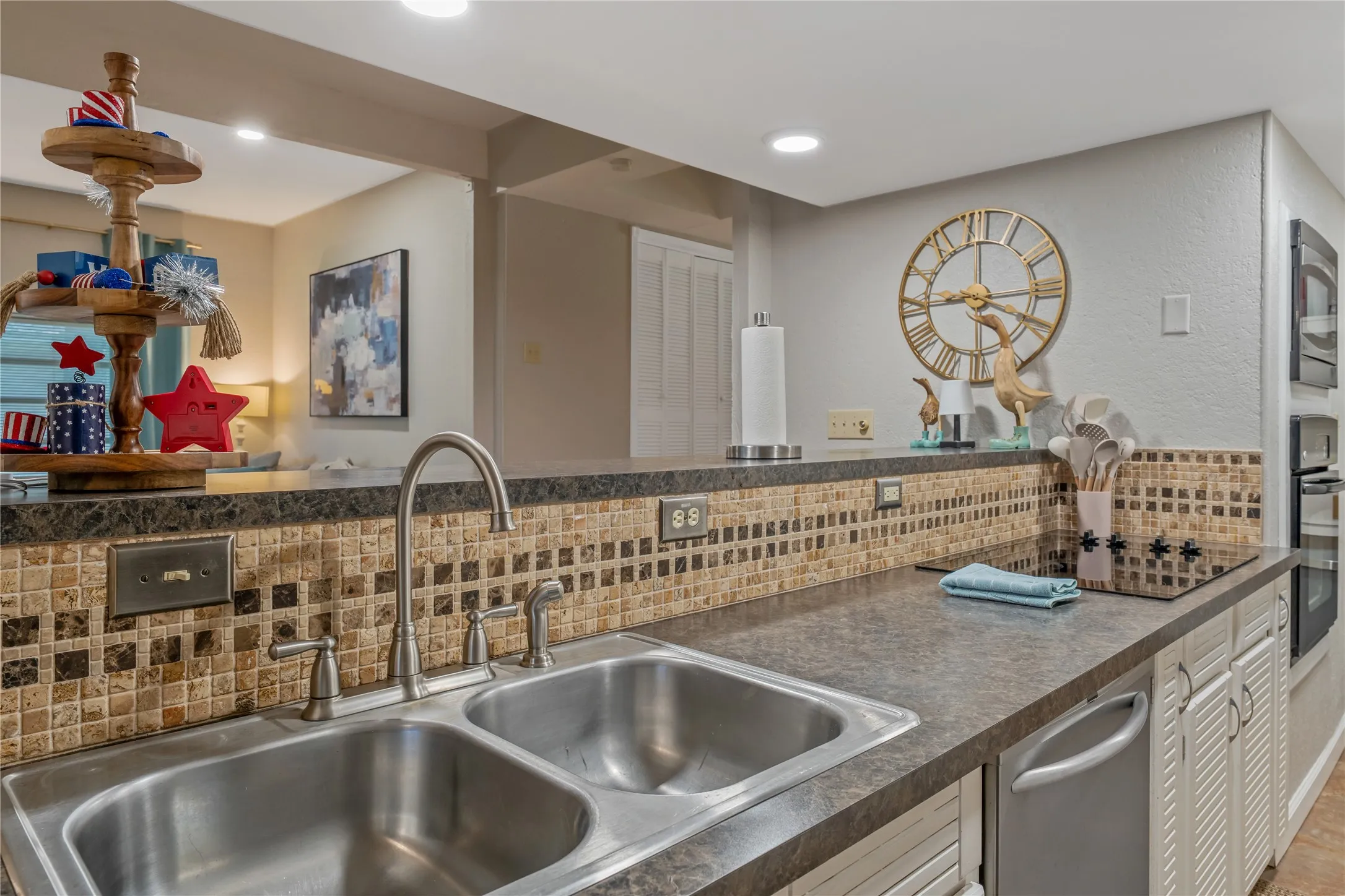 Kitchen featuring a dual basin stainless steel sink with a high-arch faucet, mosaic tile backsplash, dark-toned countertops, and a built-in cooktop