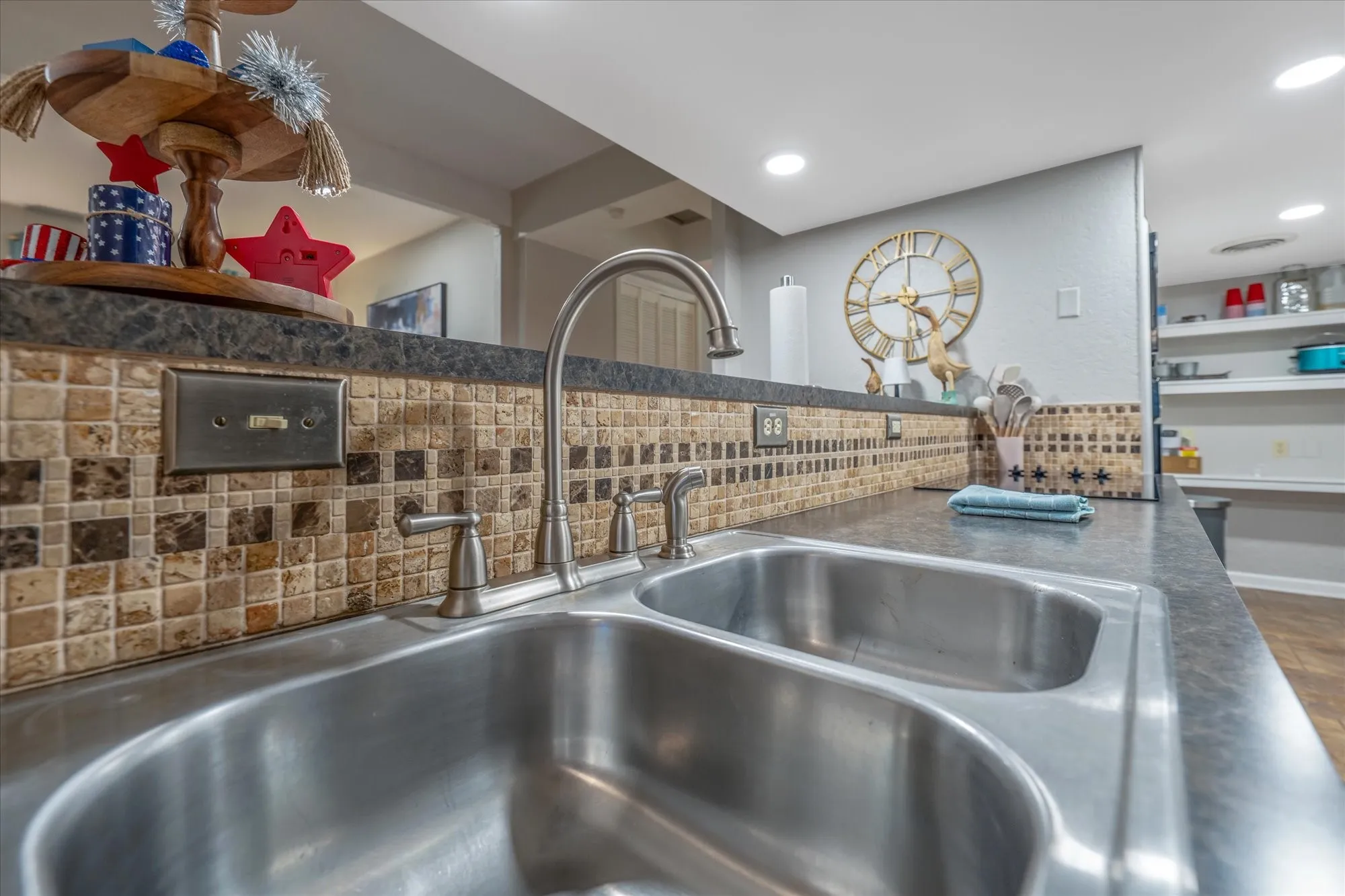Stainless steel double basin sink with a high-arch faucet, complemented by a tiled backsplash featuring varied square tiles