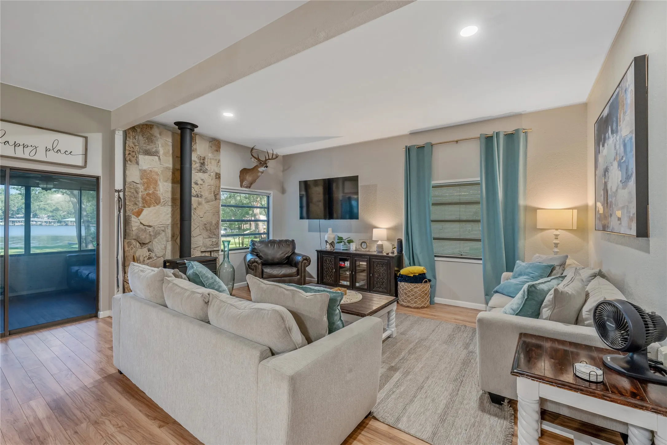 Spacious living area featuring wood-finish flooring, a stone accent wall, and a built-in wood-burning stove