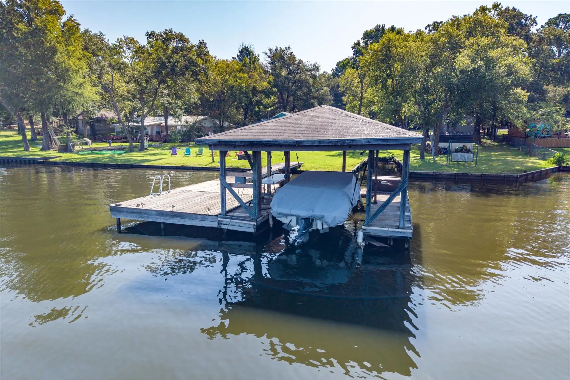 Covered boat dock featuring a wooden deck with ladder access and a boat lift