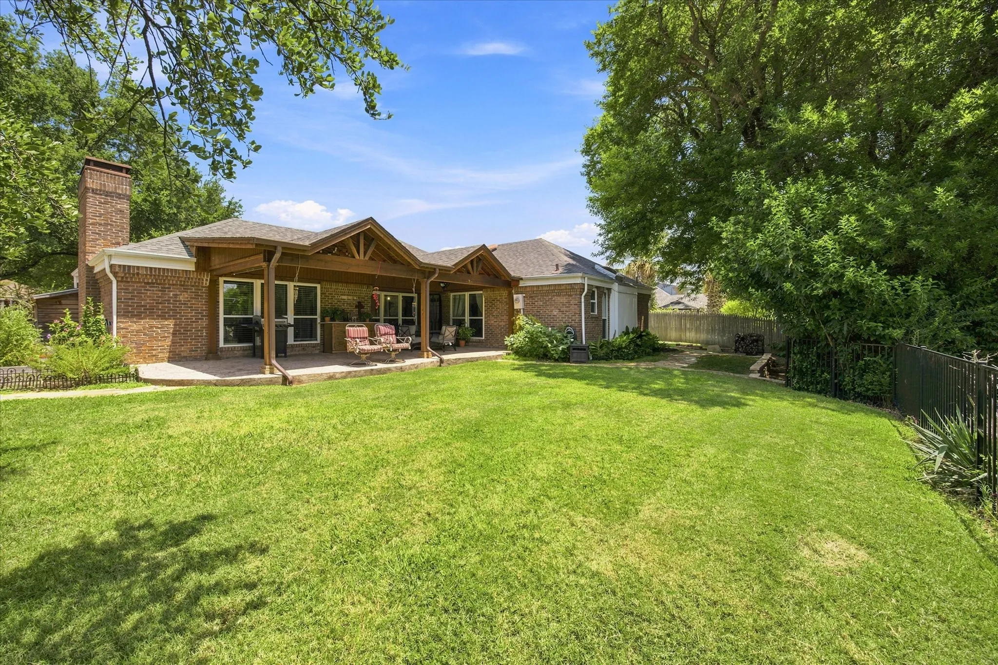 Expansive backyard with a manicured lawn, brick exterior, and covered patio