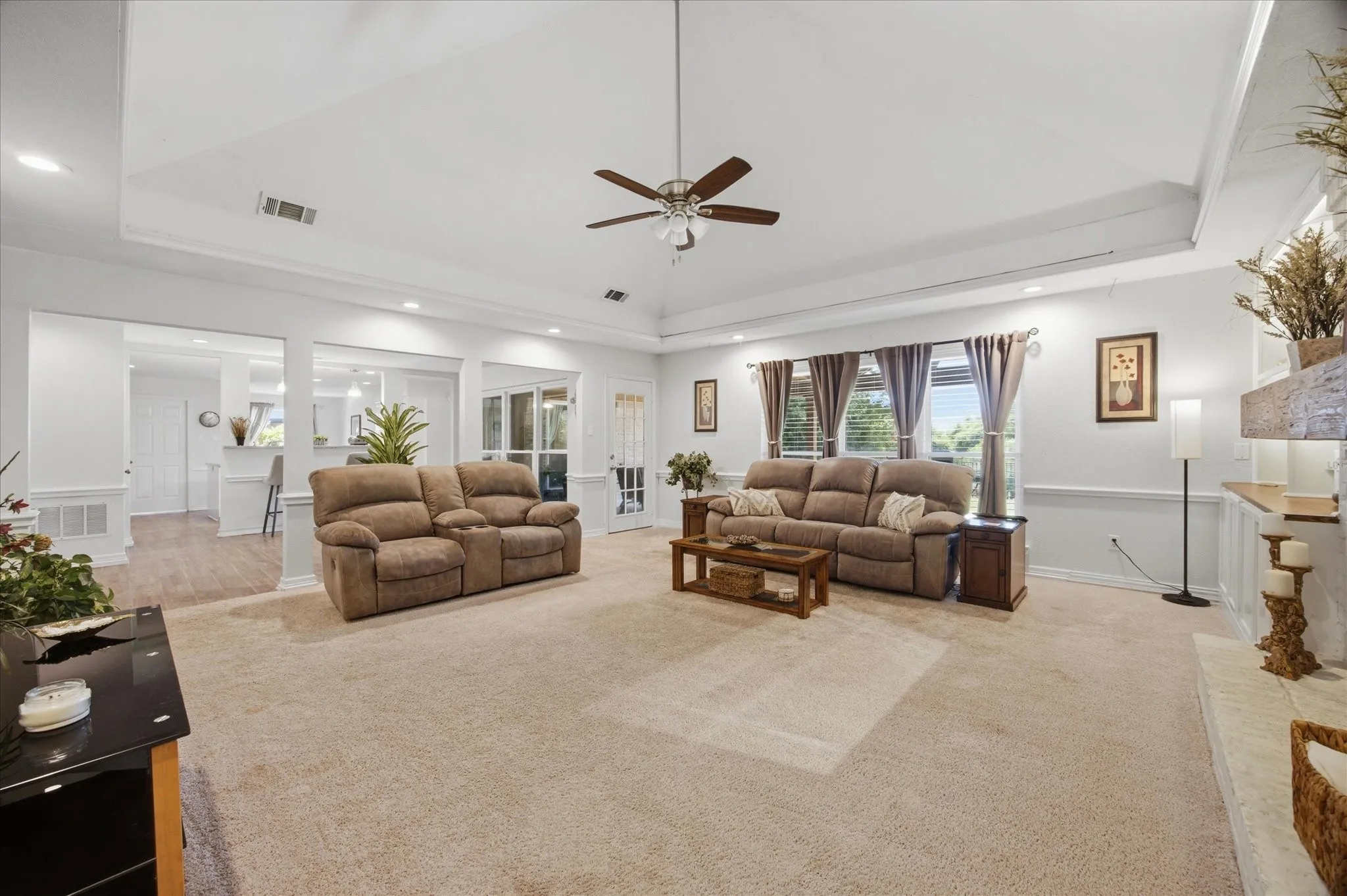 Spacious living area featuring neutral carpeting, a tray ceiling, and a ceiling fan