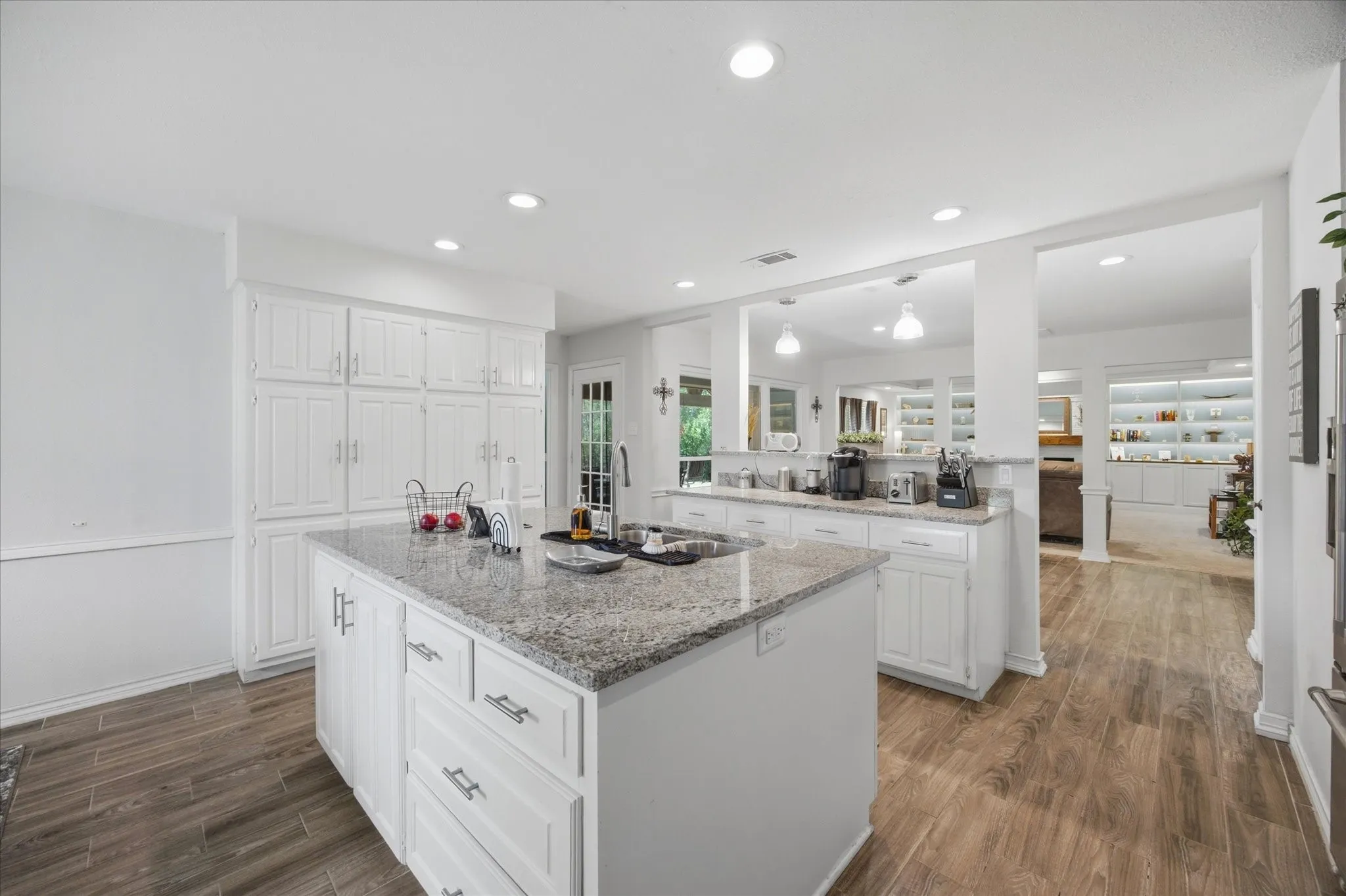 Central kitchen island with granite countertop, recessed lighting, white cabinetry, wood-finish flooring, and a built-in sink