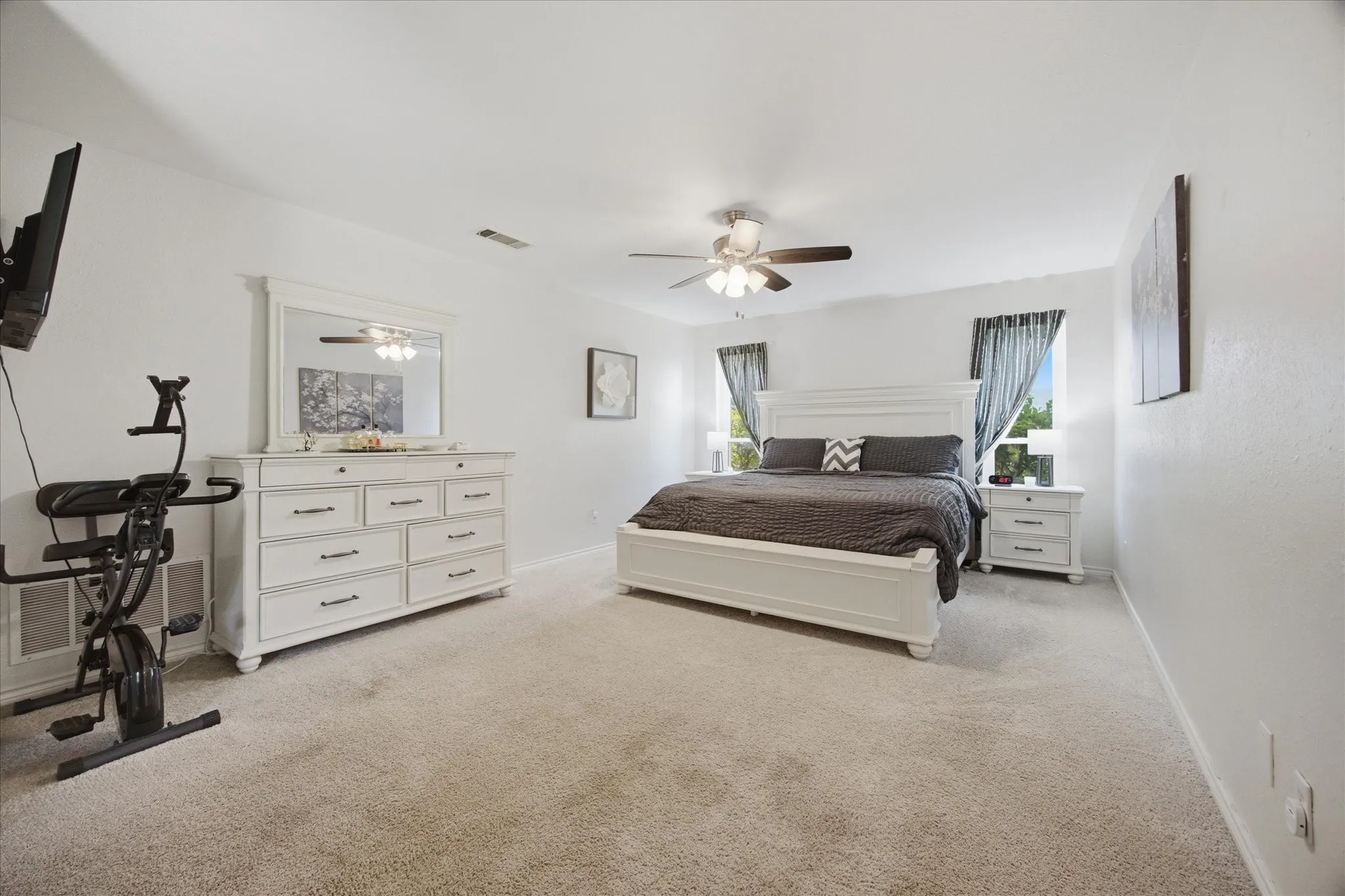 Spacious room featuring light-colored carpet, multiple windows, and a ceiling fan