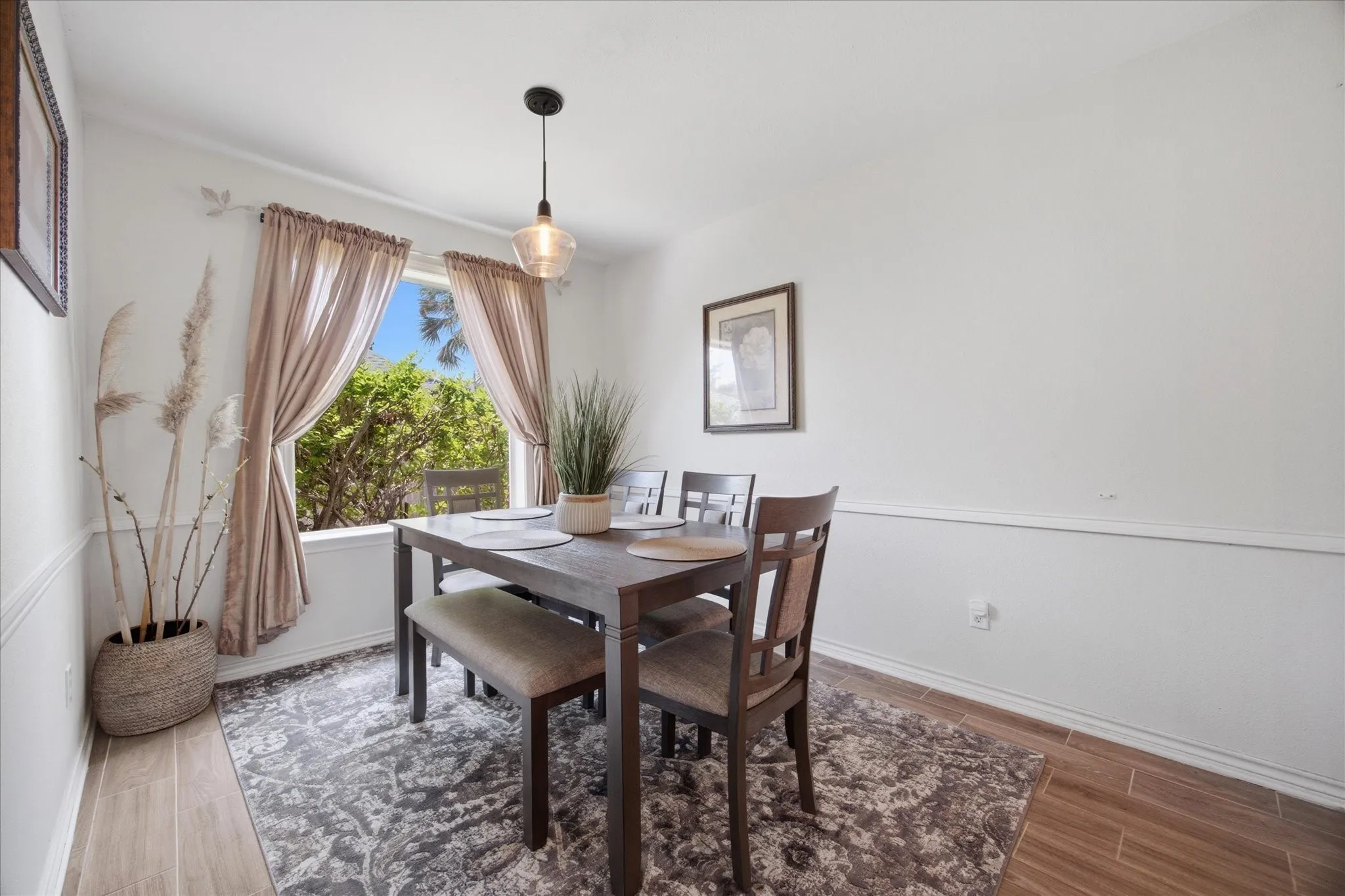 Dining area featuring wood-finish flooring, a contemporary pendant light fixture, and a picture window