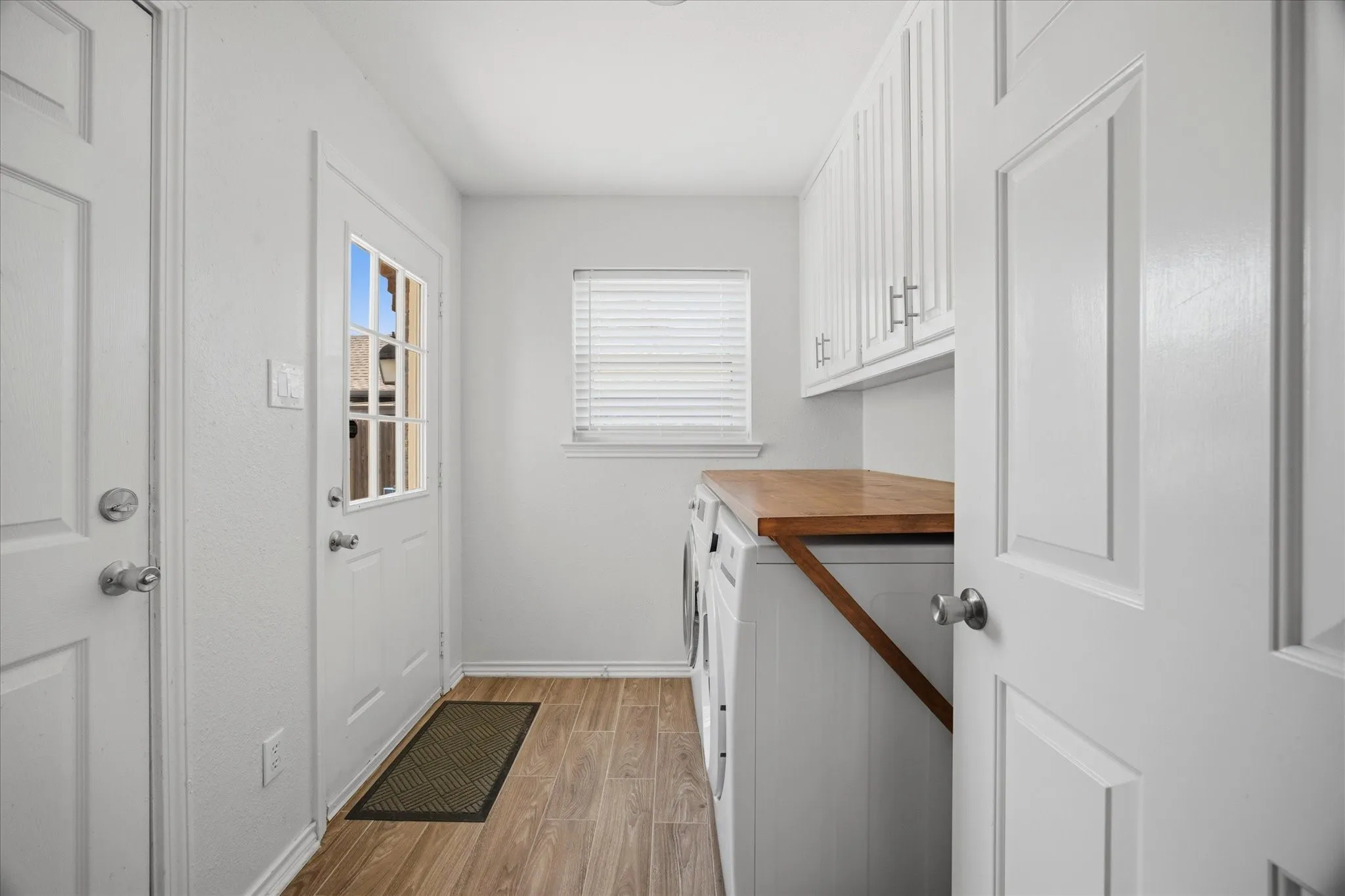 Utility room featuring wood-finish flooring, white cabinetry with silver hardware, and a wood-finish countertop