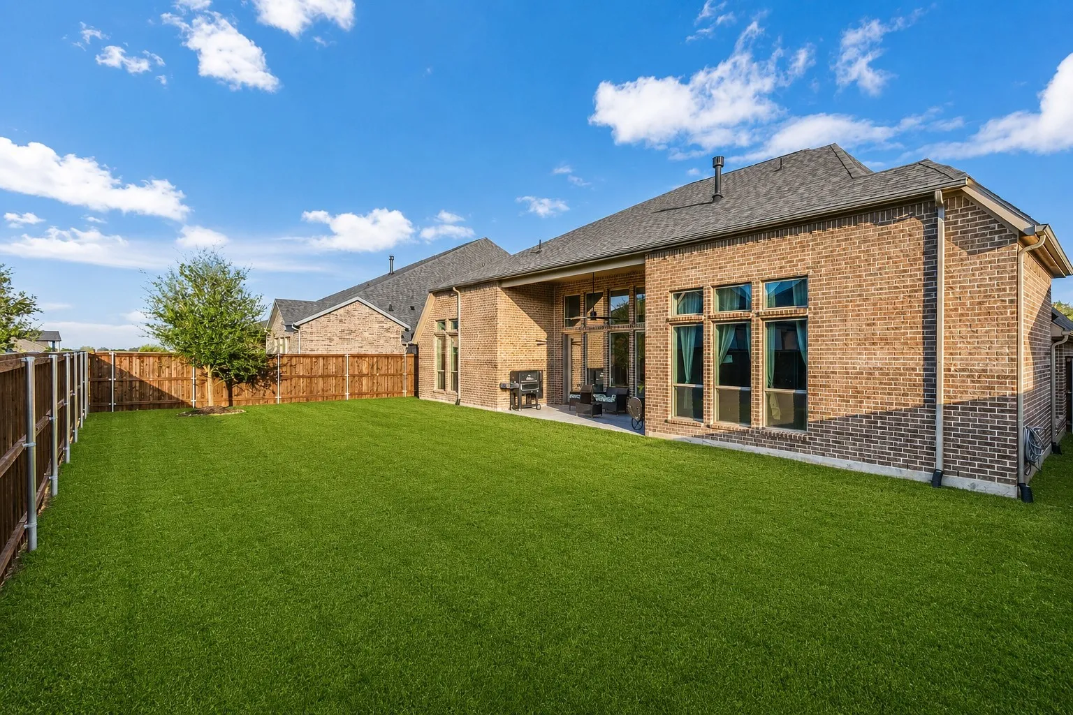 Expansive backyard featuring a lush lawn, privacy fencing, and a covered patio area